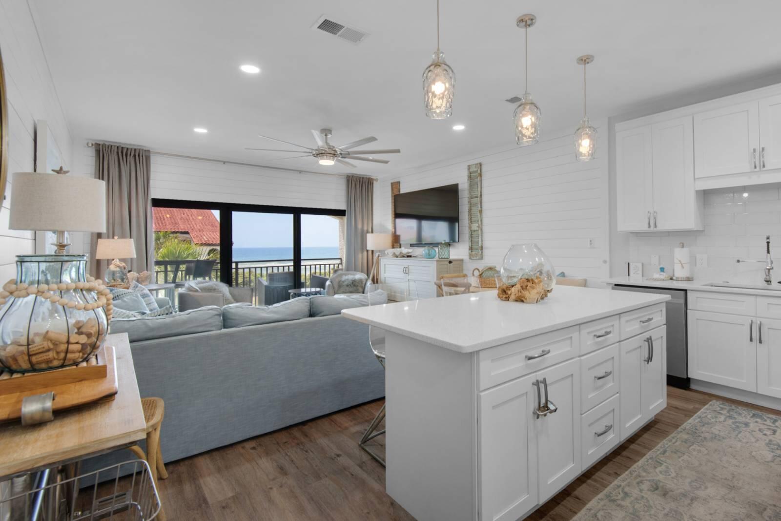 Open-plan kitchen and living room with a large white island and water visible through sliding glass doors.