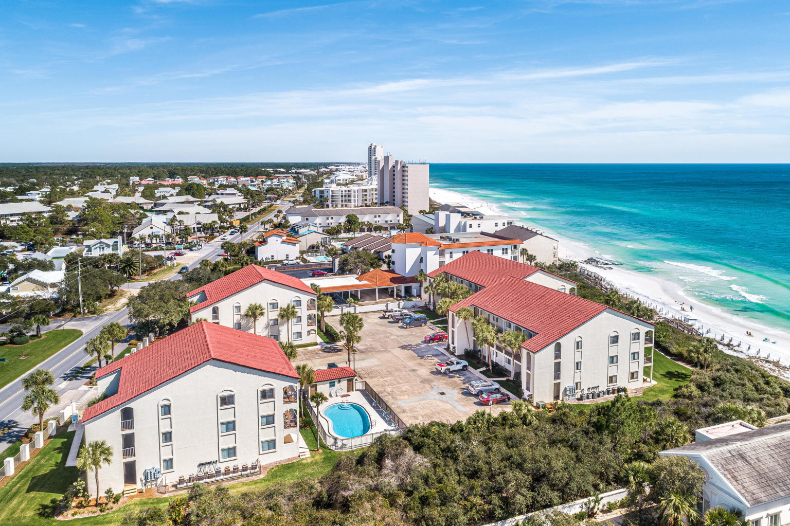 Beachfront condominium complex with a courtyard pool, sandy shore, and turquoise Gulf water.