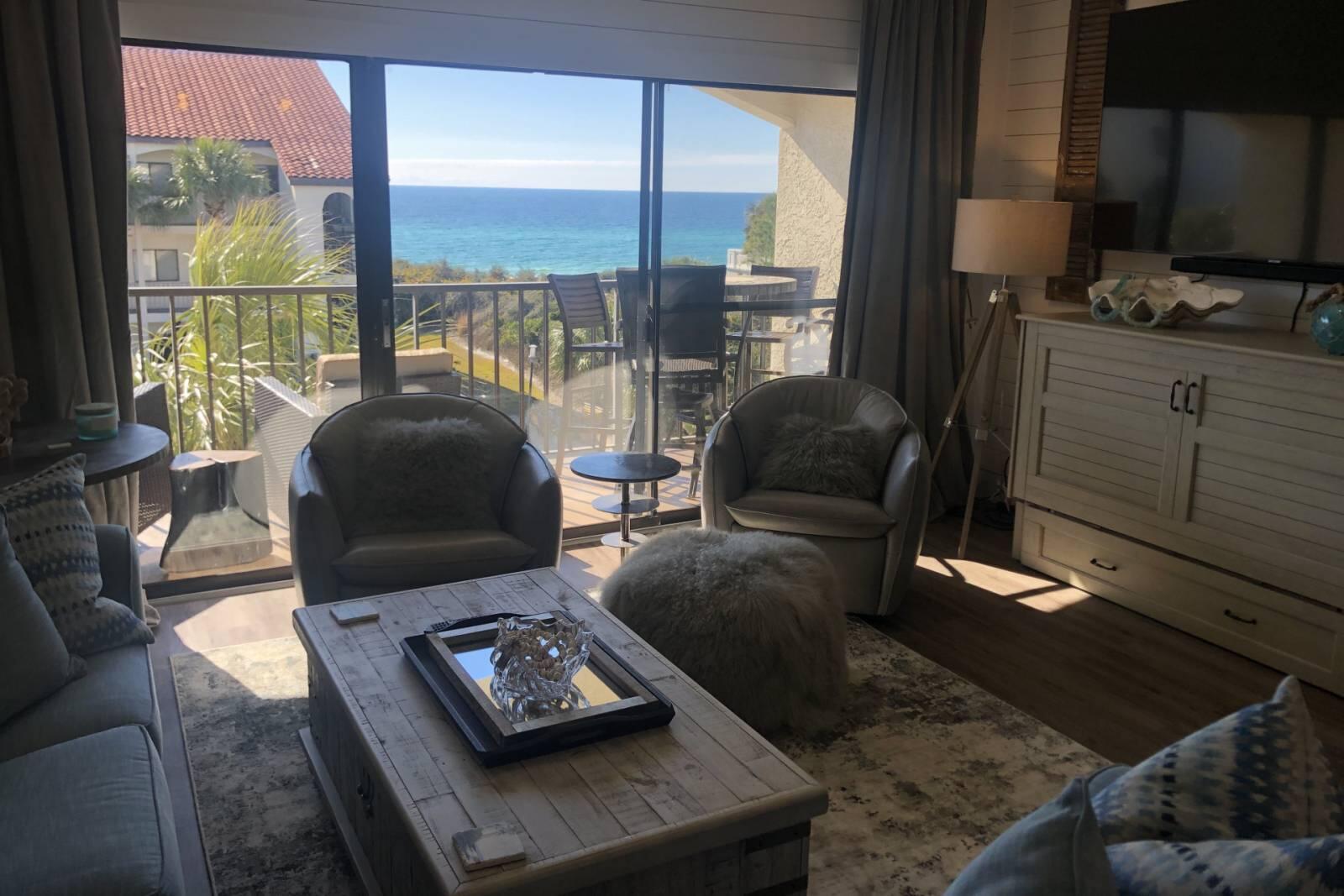 Living room with gray seating and a balcony overlooking the ocean.