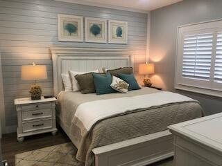 Bedroom with a white paneled bed, teal accent pillows, and plantation shutters.