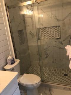 Bathroom with a glass shower, marble-look tile, patterned mosaic niche, and toilet beside a light vanity.