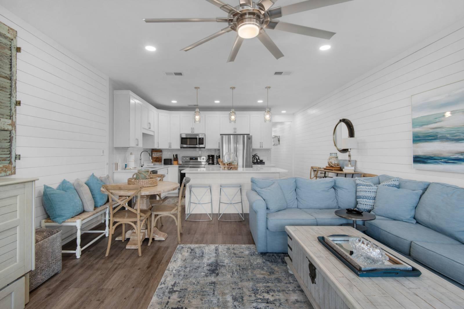 Open-plan living room and kitchen with a blue sectional, white cabinetry, and stainless steel appliances.