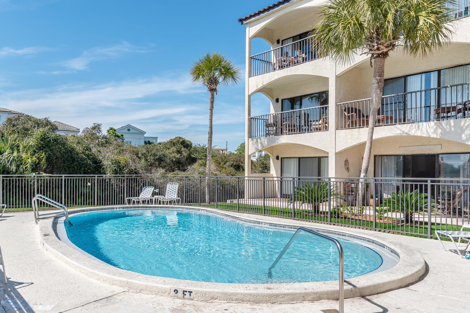 Outdoor pool beside a condominium with arched balconies and palm trees.