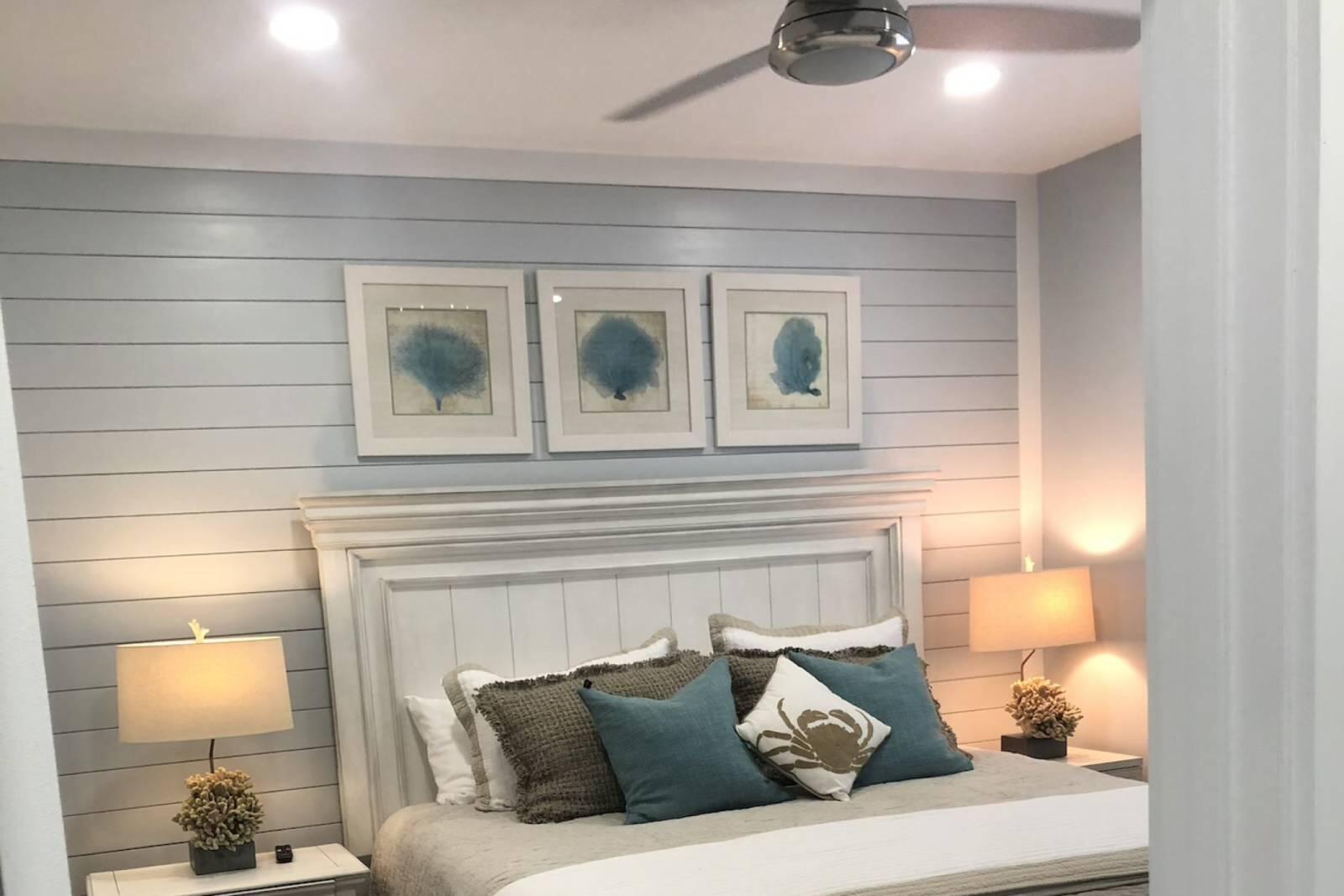 Bedroom with a gray shiplap accent wall, framed prints, and a bed layered with teal pillows.