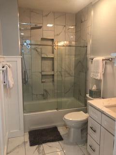 Bathroom with glass-enclosed tub and shower, white vanity, and tiled floor.