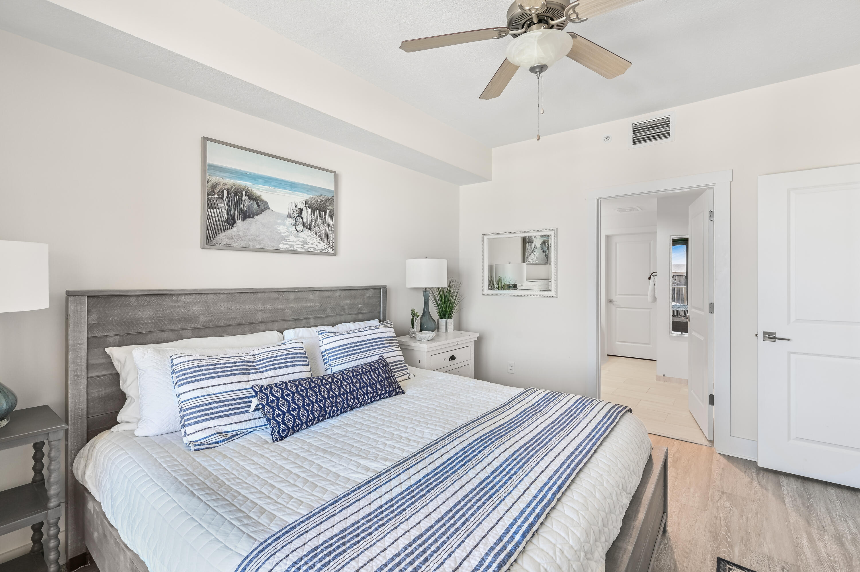 Bedroom with a large bed, blue-and-white striped bedding, gray wood headboard, and beach-themed wall art.