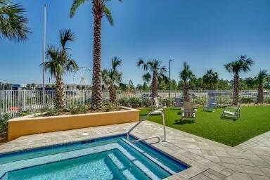 Outdoor pool with tiled steps beside a palm-lined artificial-turf lawn and lounge chairs.