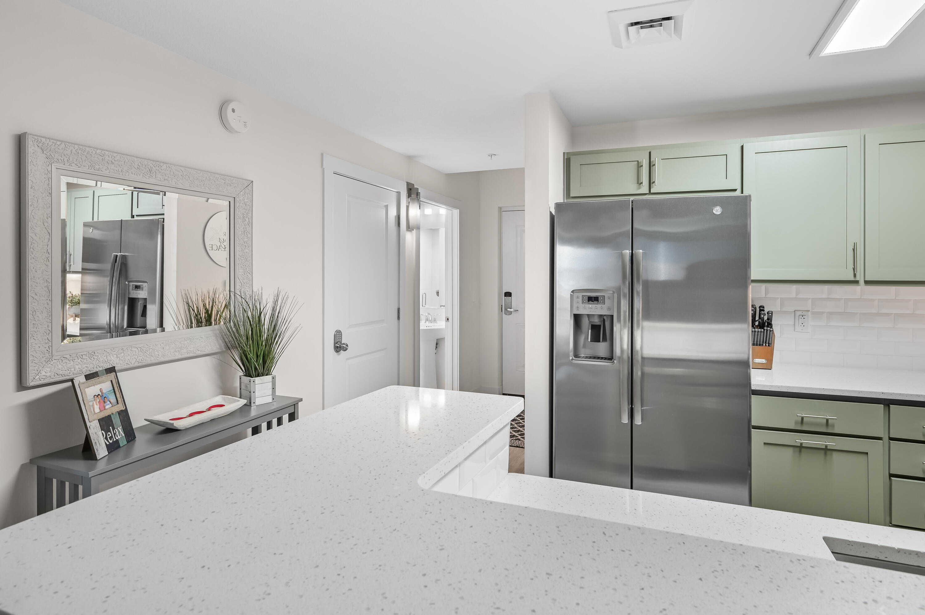 Condo kitchen with pale green cabinets, a stainless steel refrigerator, and a large white island.