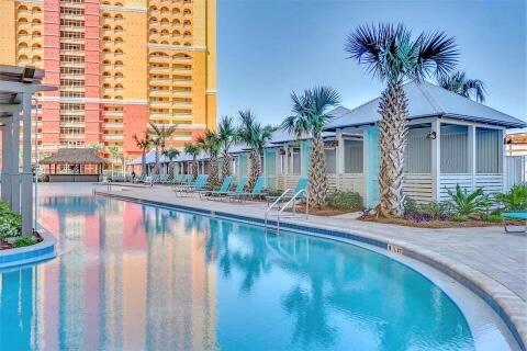 Resort pool beside a high-rise condominium, with palm trees and a poolside pavilion.