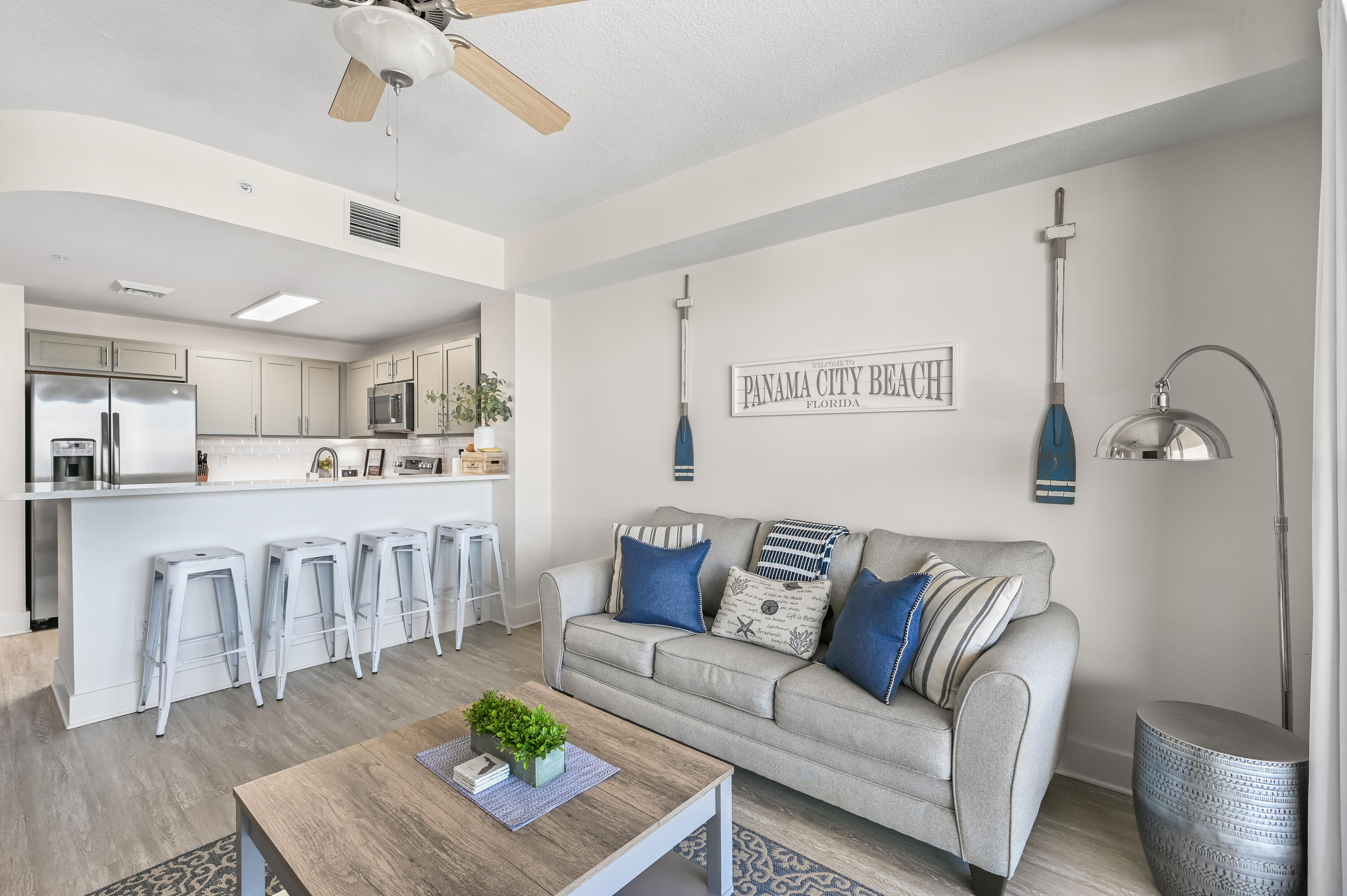 Staged living room with a gray sofa, blue accents, and an open kitchen with breakfast bar.
