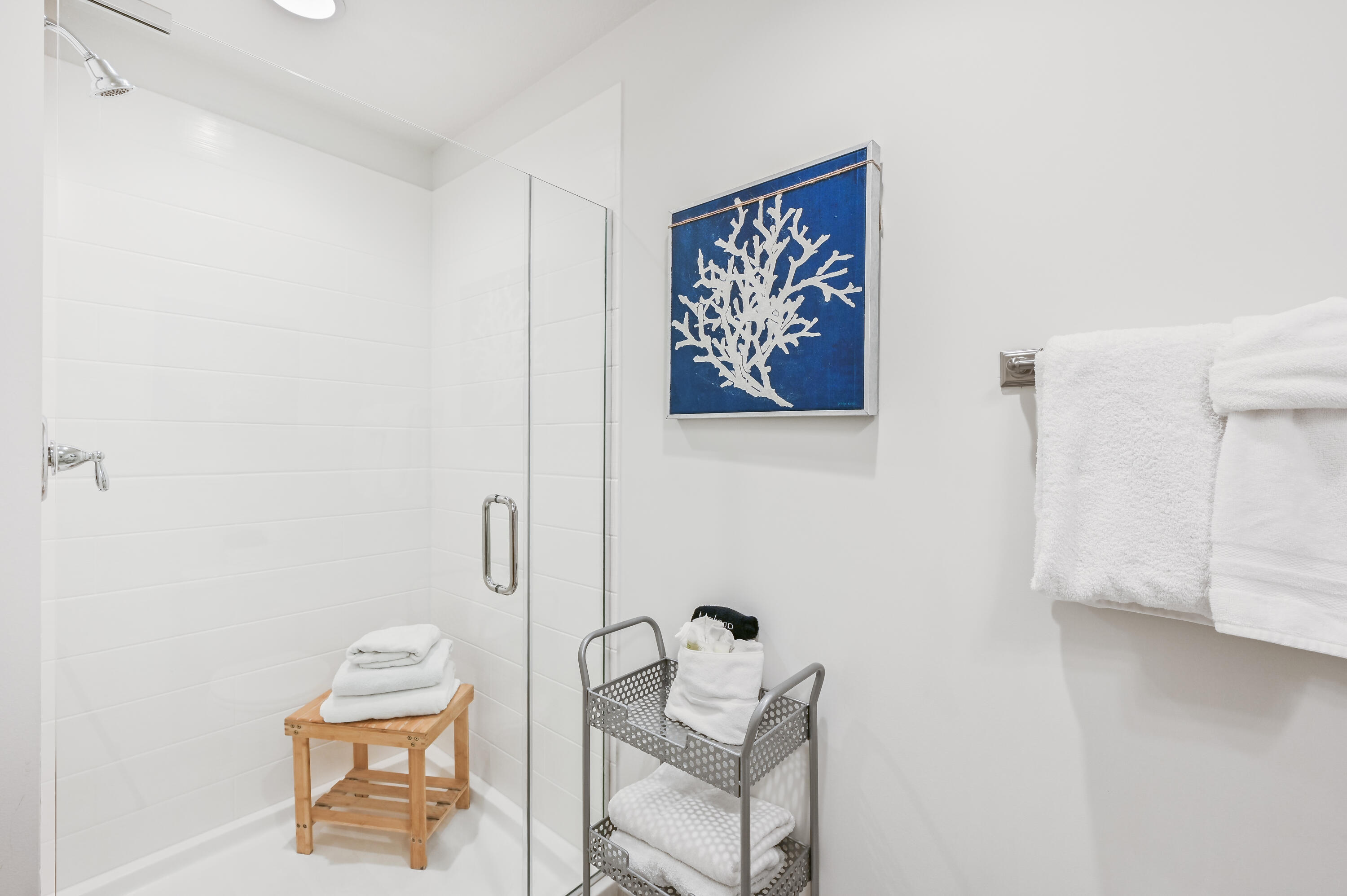 Bright bathroom with a glass shower, white towels, and blue coral artwork.