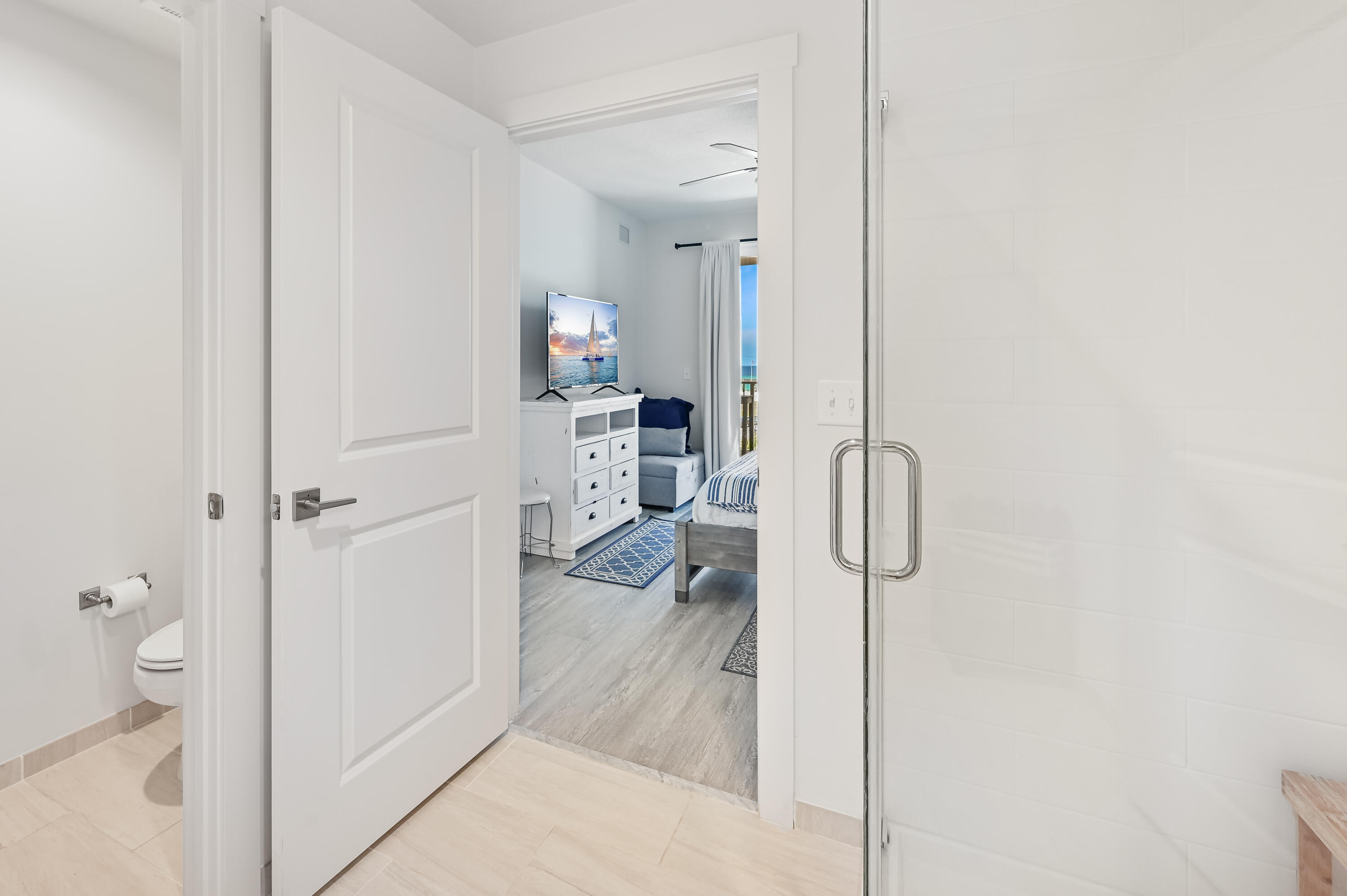 Bathroom with a glass shower and toilet opening onto a bedroom with blue accents.