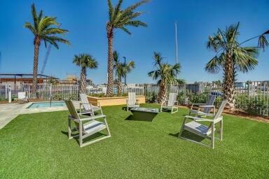 Condominium outdoor lounge area with white chairs on a lawn, palm trees, and a pool.