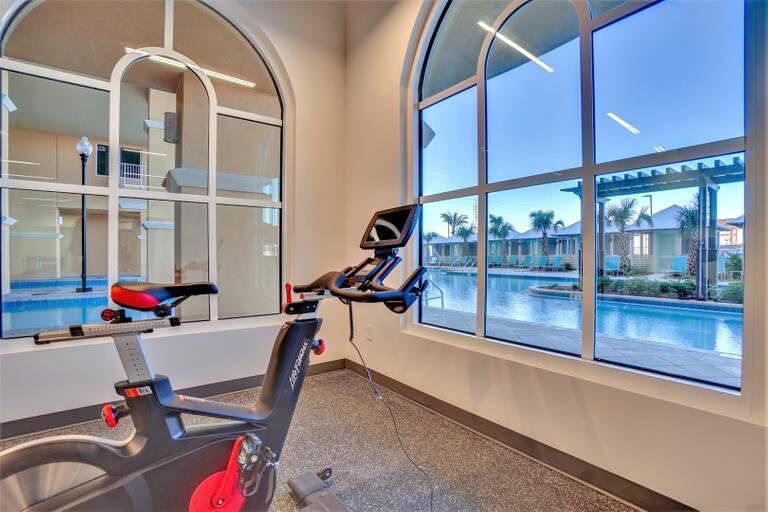Fitness room with exercise equipment and large windows overlooking the pool.