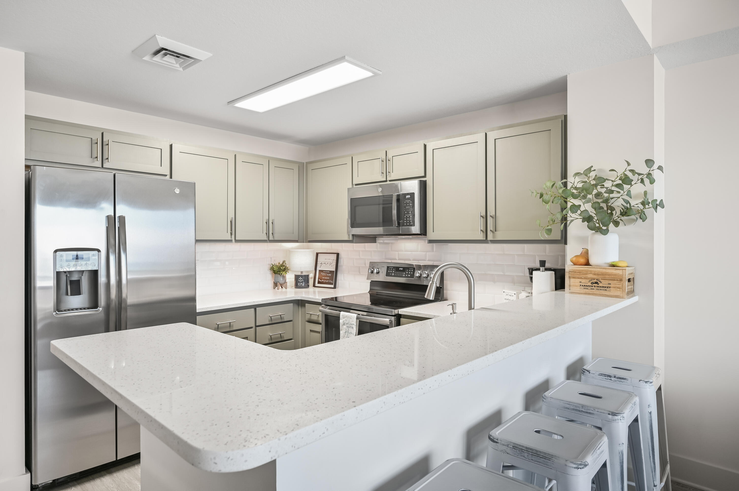 Kitchen with a large white quartz peninsula, pale cabinets, and stainless steel appliances.