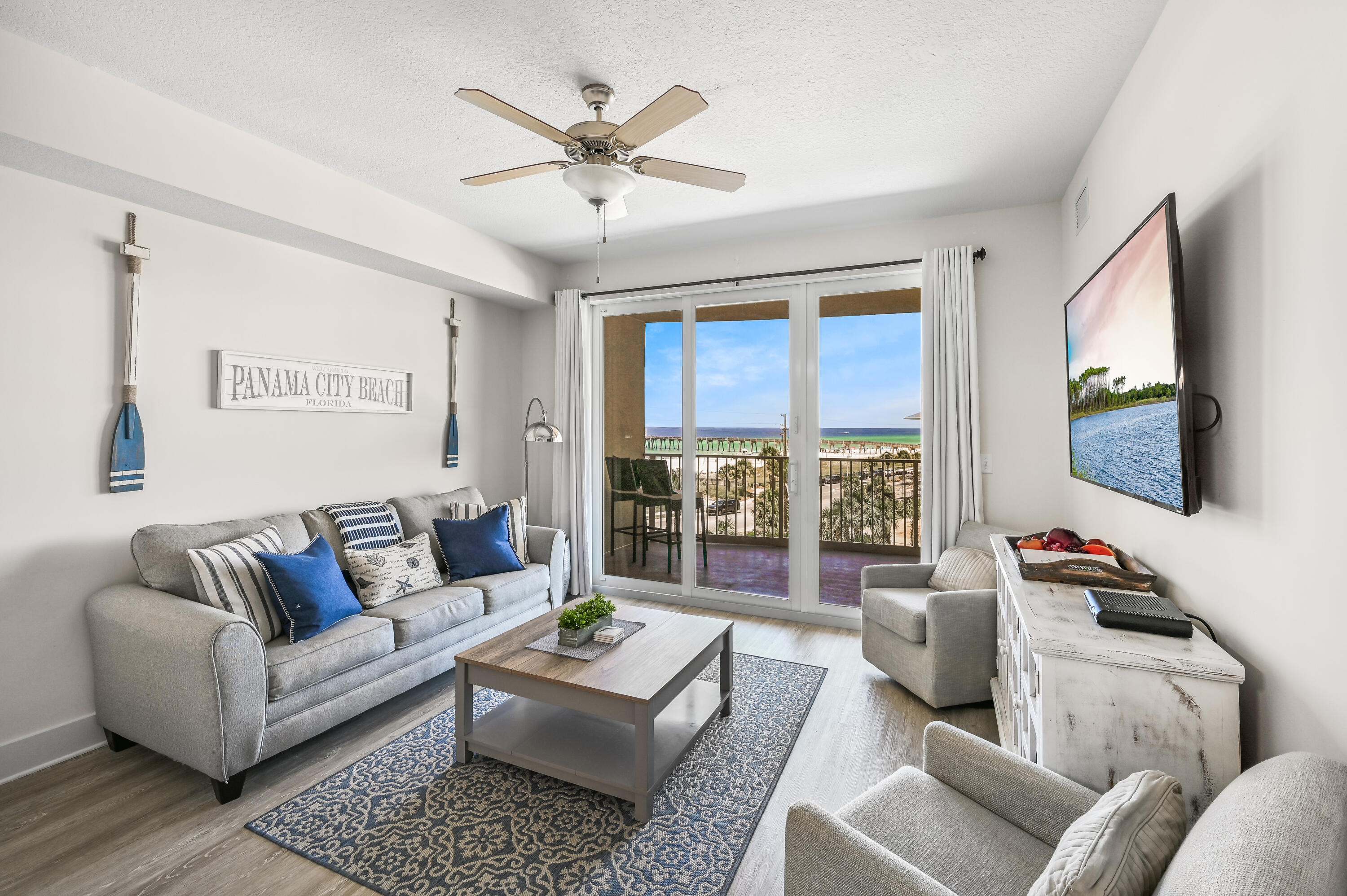 Furnished living room with blue-and-gray seating and sliding doors overlooking the beach and ocean.