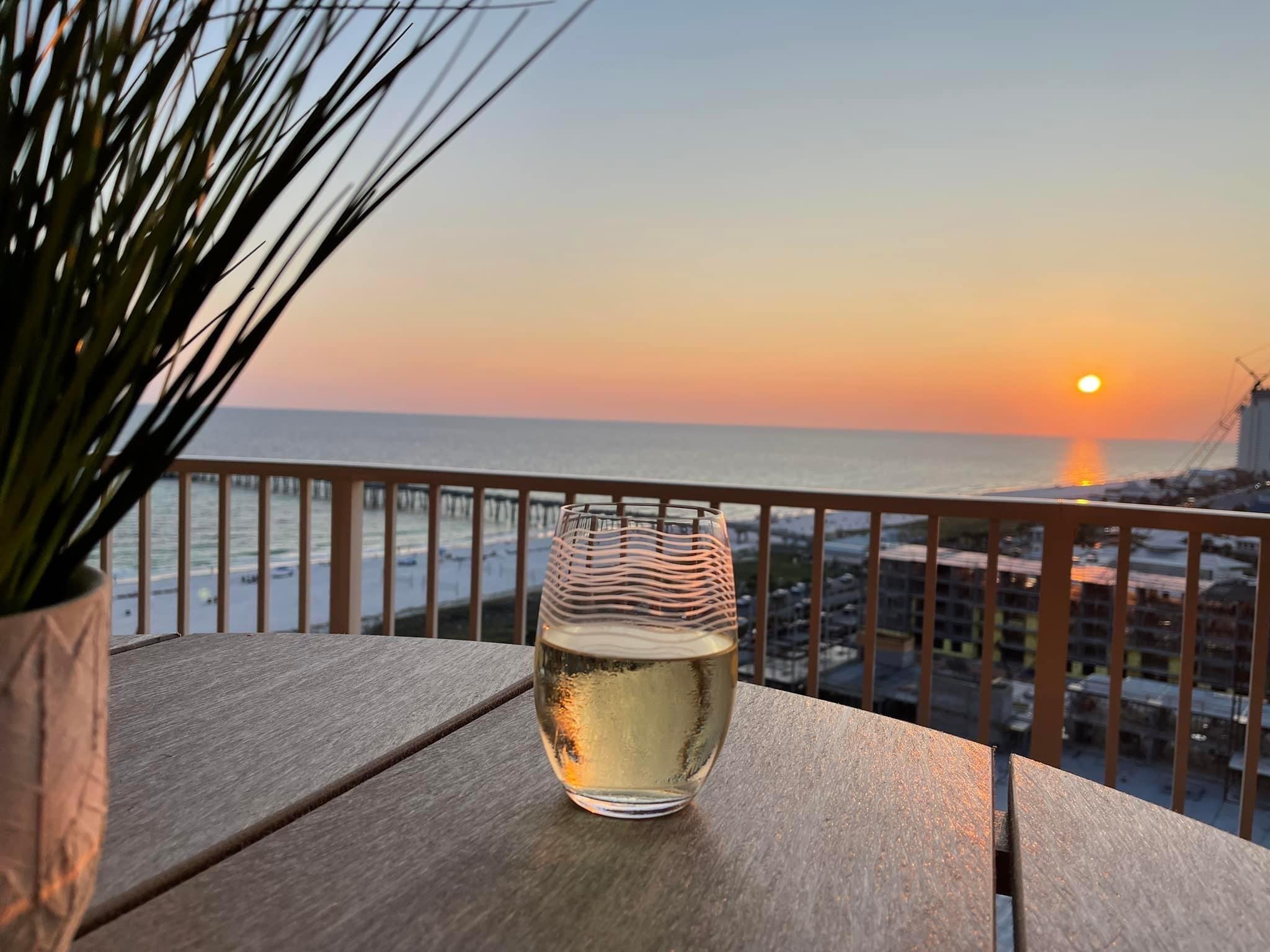 Balcony table overlooking the water at sunset, with a glass of wine in the foreground.