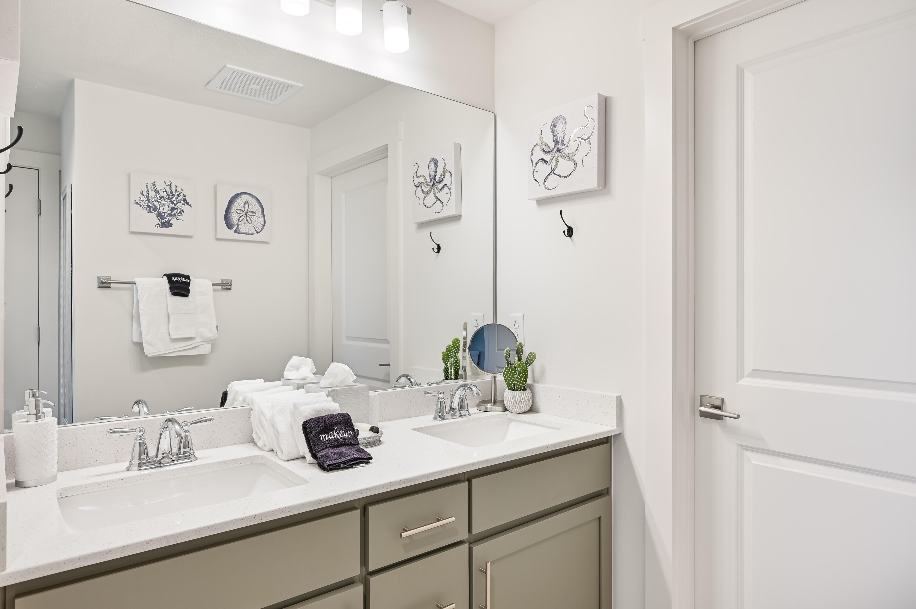 Bathroom vanity with two sinks, a large mirror, folded towels, and coastal wall art.