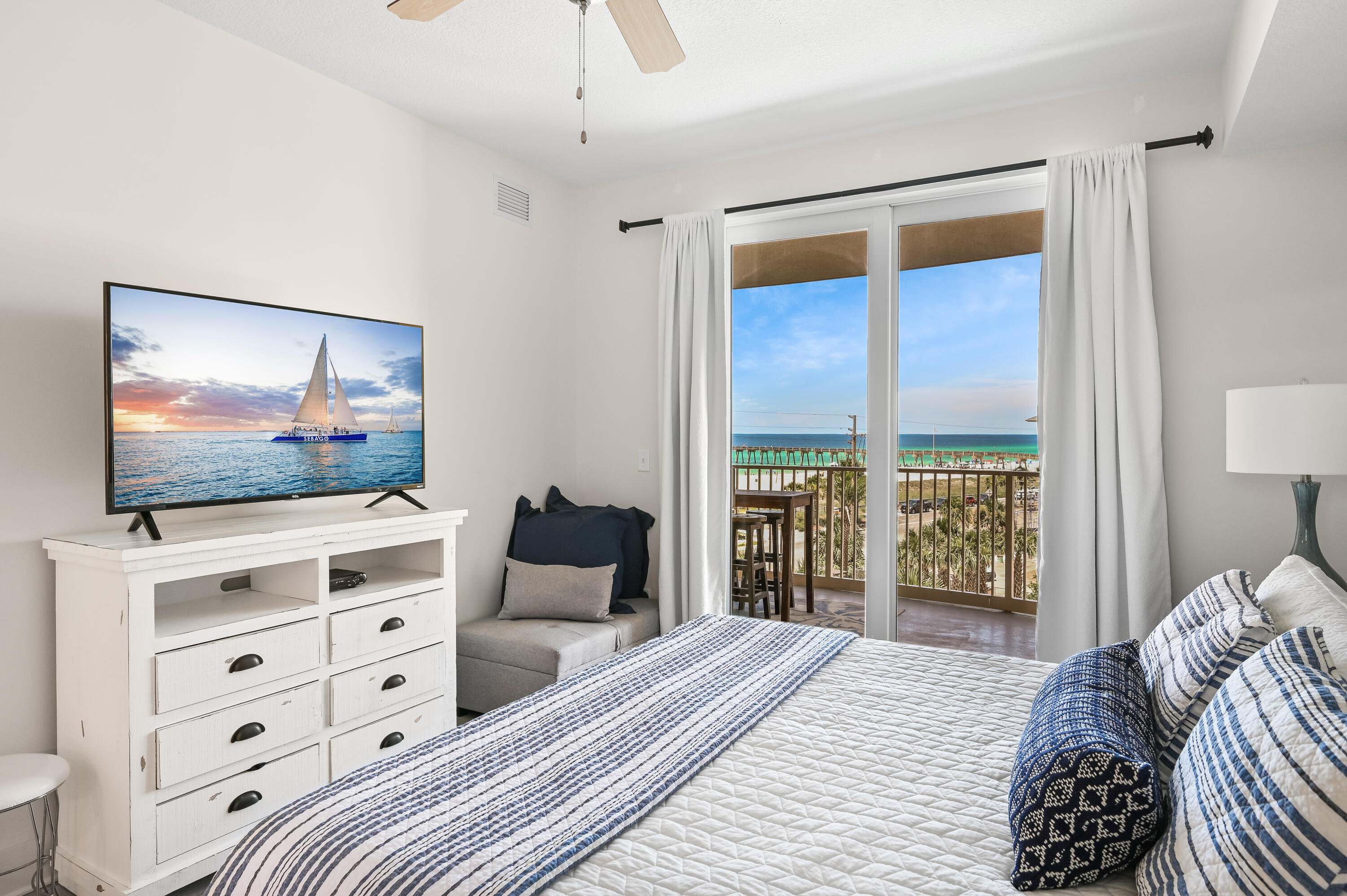 Bedroom with blue-and-white bedding and a balcony view of the beach and turquoise water.
