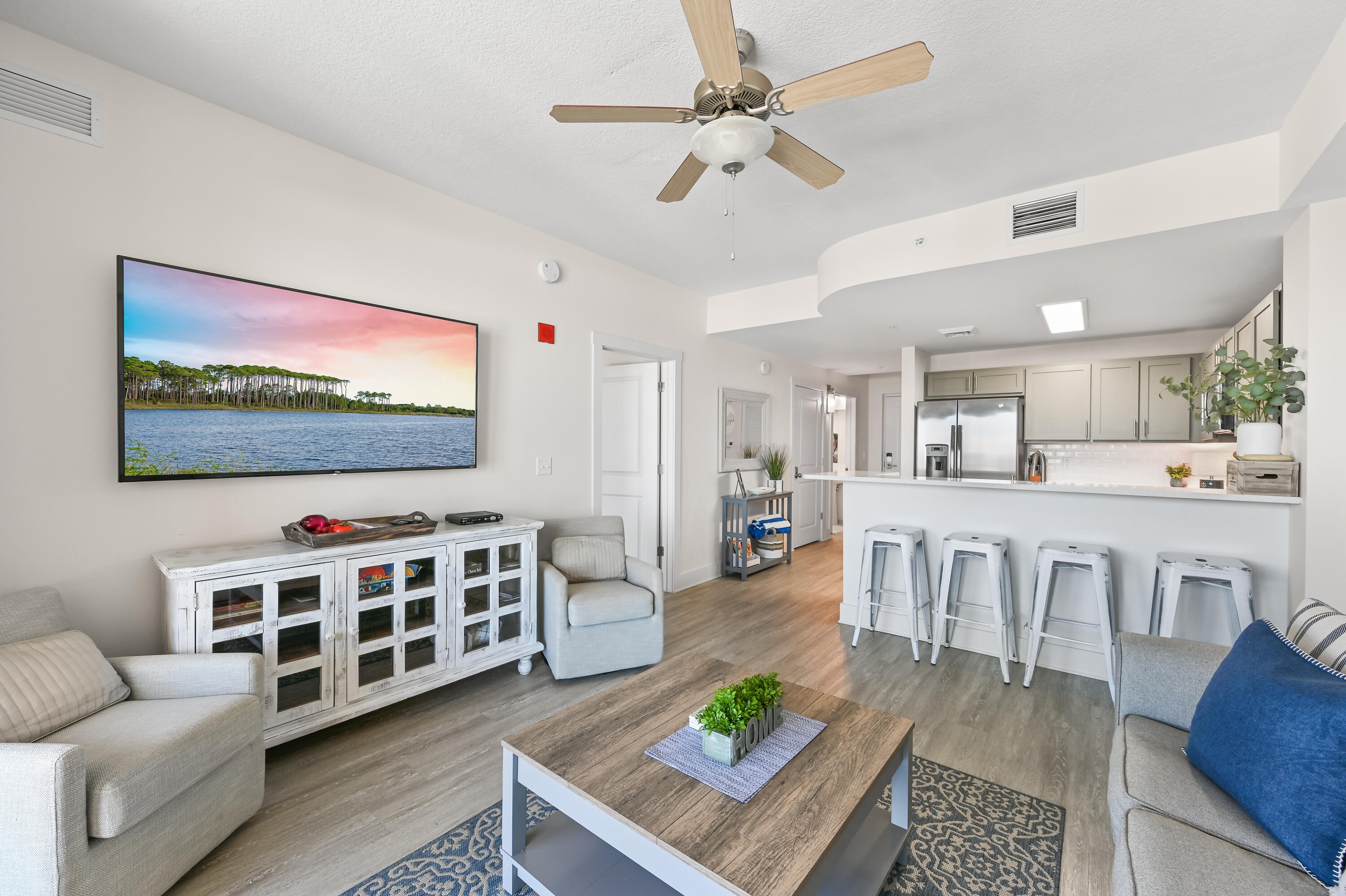 Open-plan condo living room and kitchen with a breakfast bar, stainless appliances, and light upholstered seating.