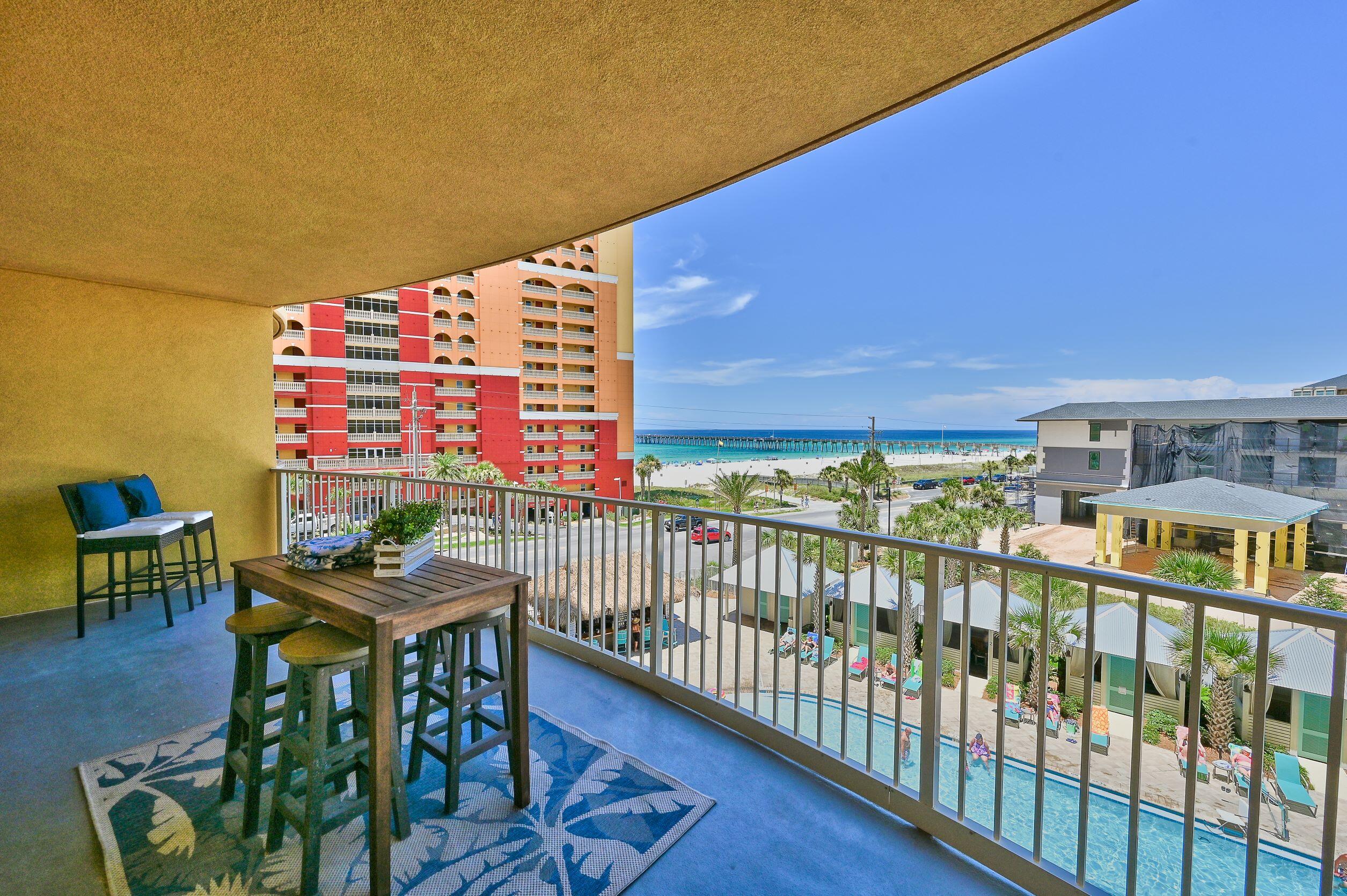 Condominium balcony with outdoor dining furniture overlooking a pool, beach, Gulf, and pier.