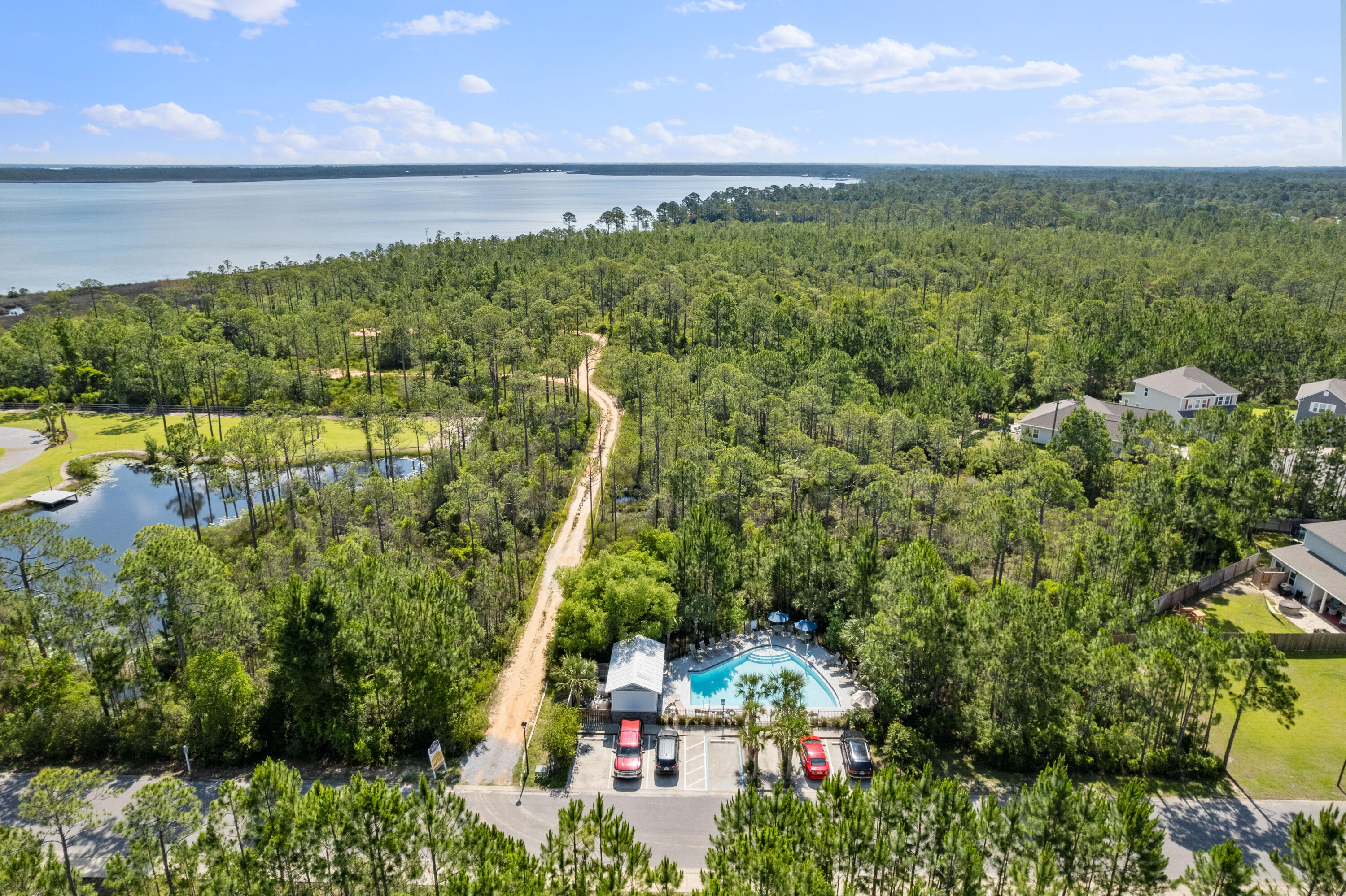 Aerial view of wooded coastal community, bay, winding road, neighborhood pool, and pond.