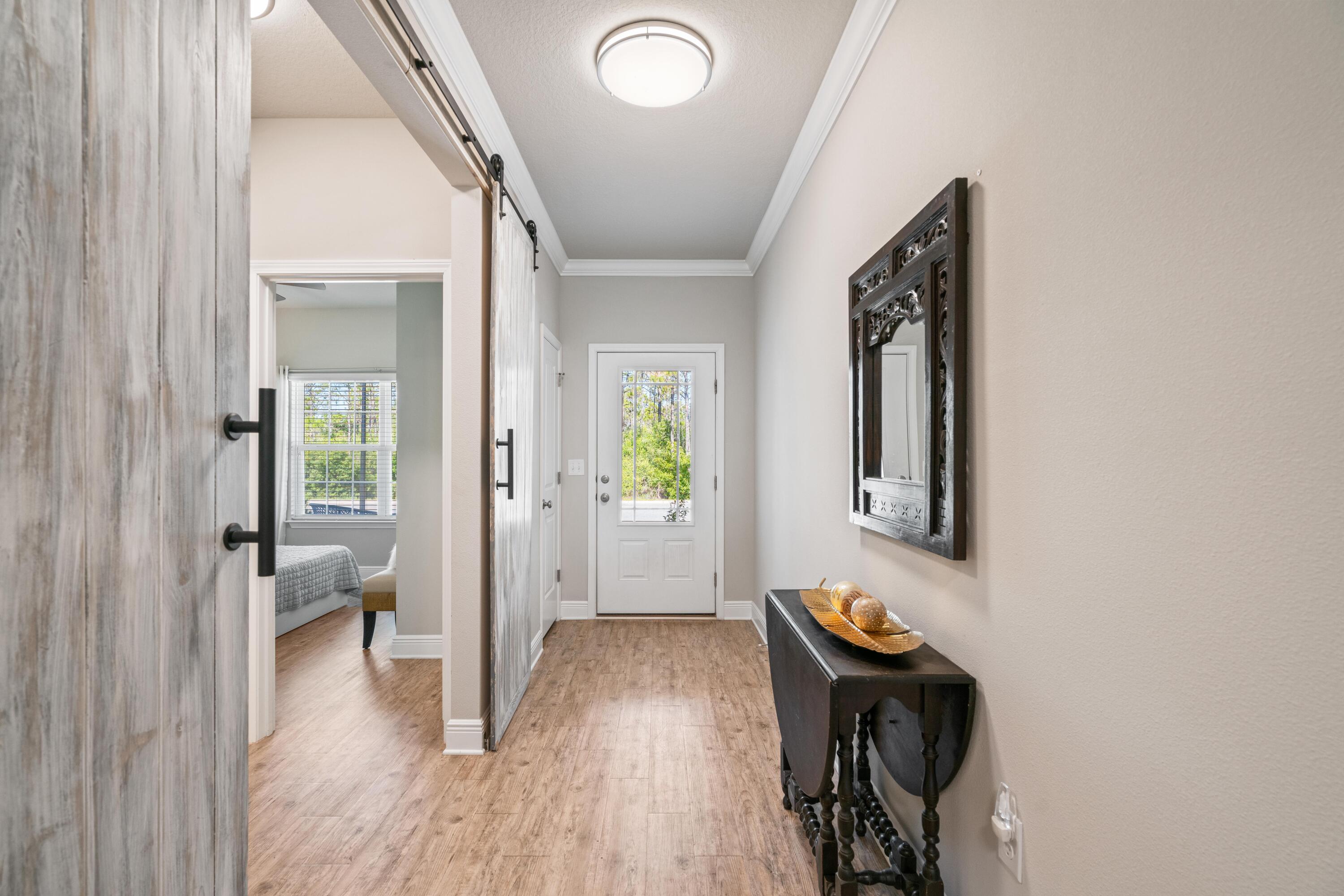 Entry hall with a glass-panel front door, wood-look flooring, and a barn door opening toward a bedroom.