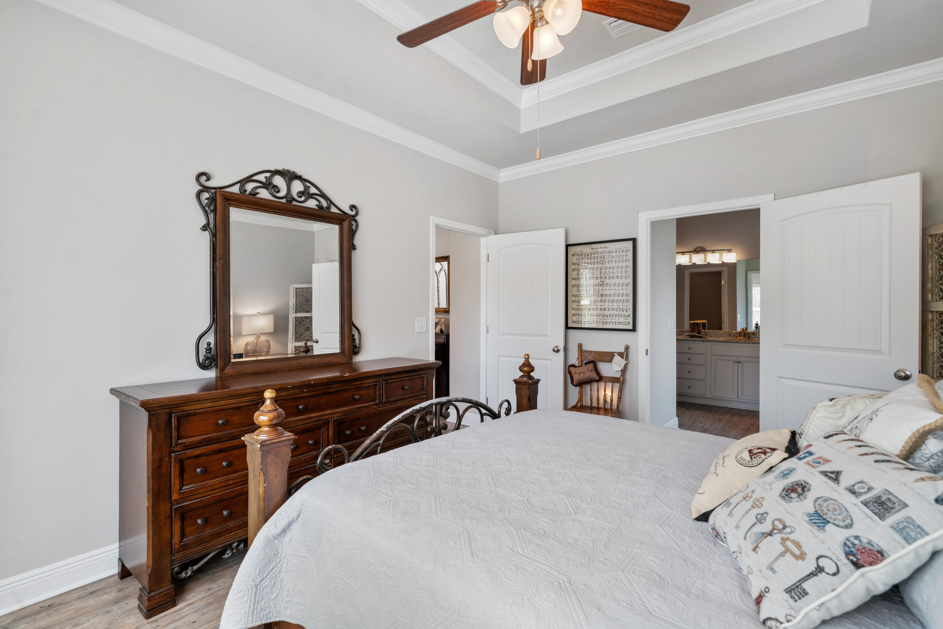 Bedroom with a white quilted bed, ornate dark wood dresser and mirror, and an open en-suite bathroom doorway.