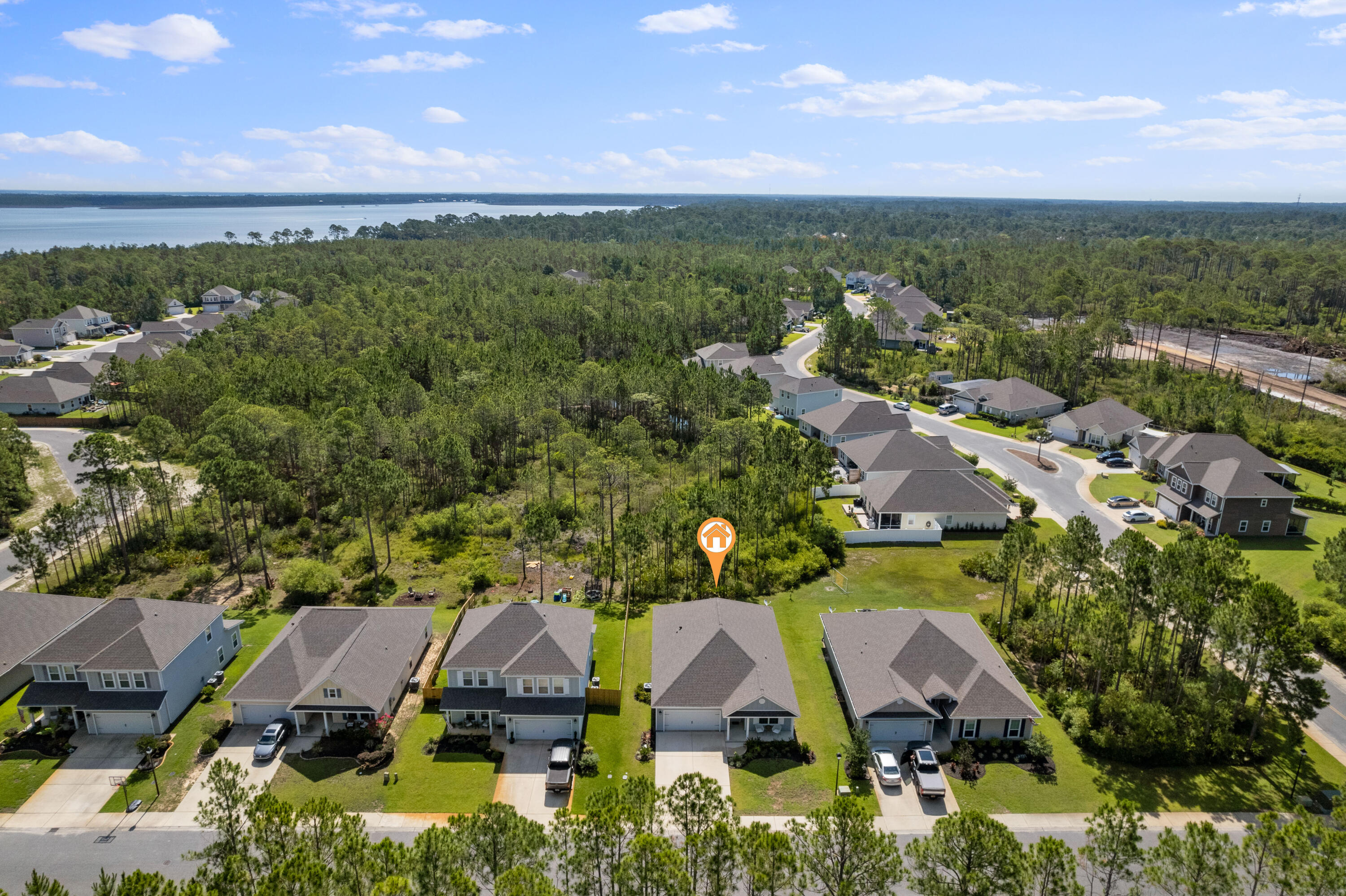 Aerial view of a wooded homesite in a neighborhood, with water visible beyond the trees.