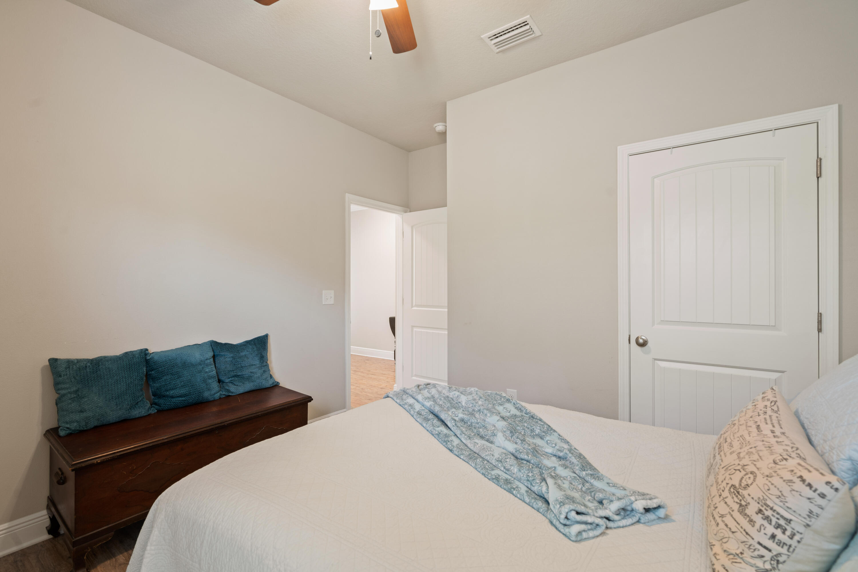 Bedroom with a white bed, blue throw, and dark wooden bench with teal cushions.