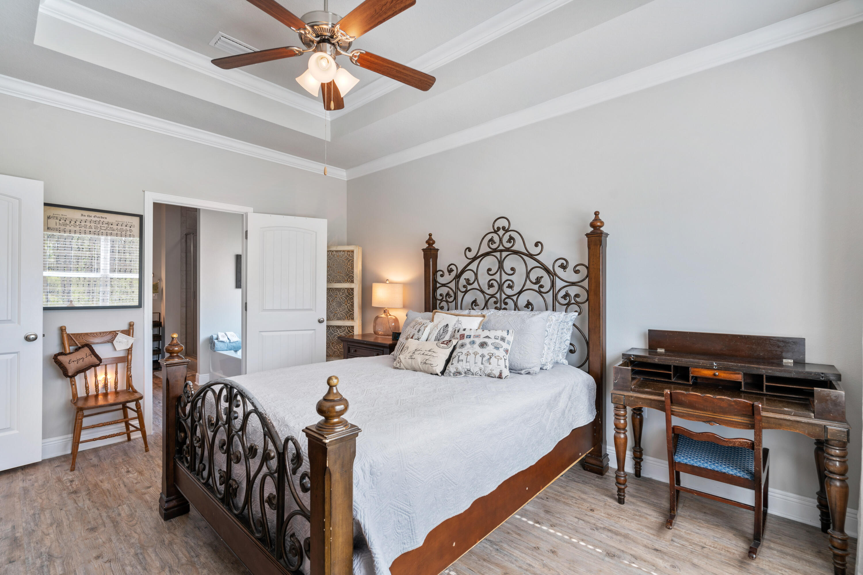 Furnished bedroom with an ornate iron-and-wood bed and antique-style desk beneath a tray ceiling.