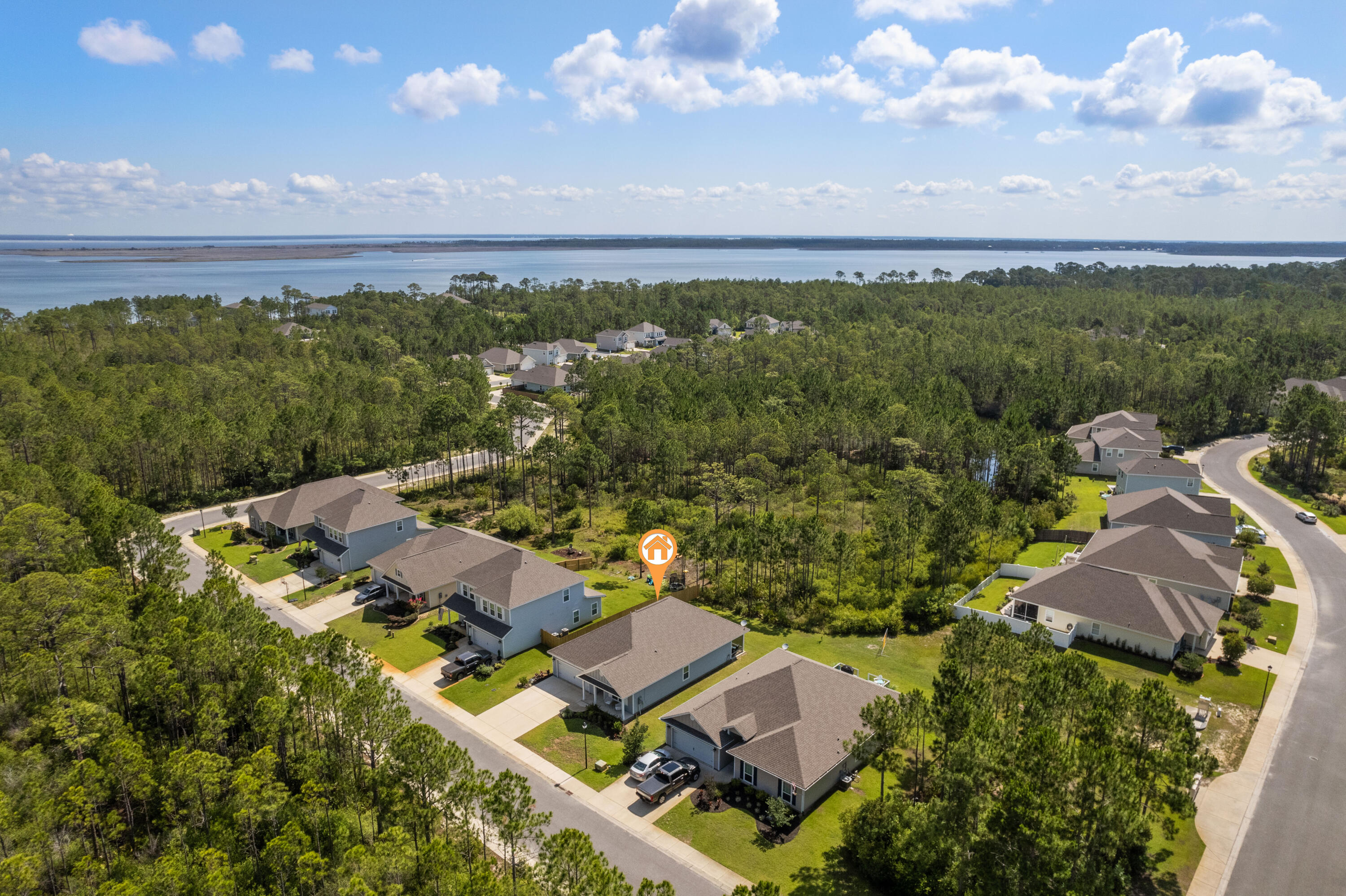 Aerial view of homes among pine woods, with the bay in the distance and an orange marker at the featured property.