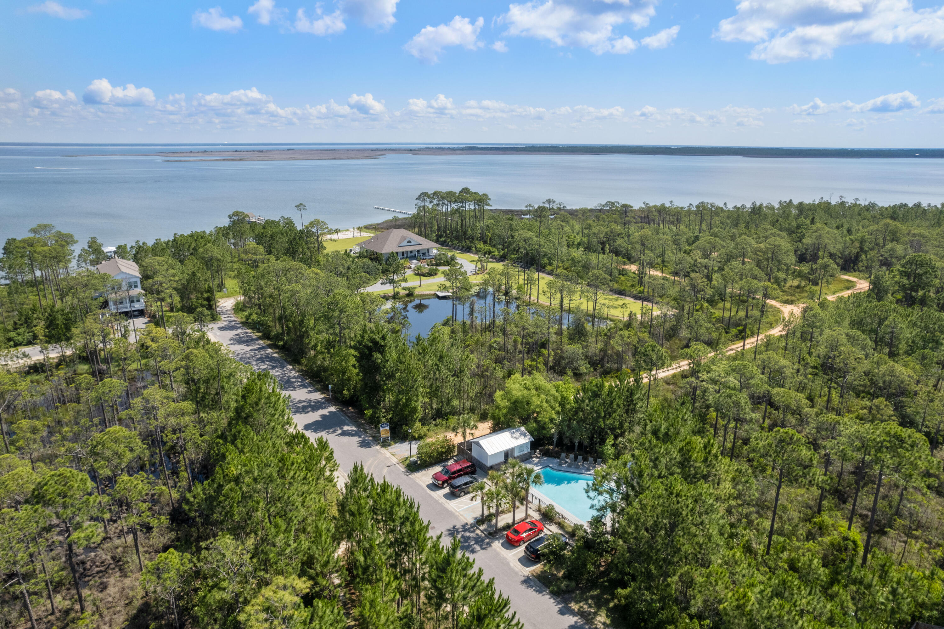 Aerial view of wooded homes and a swimming pool beside a broad bay.