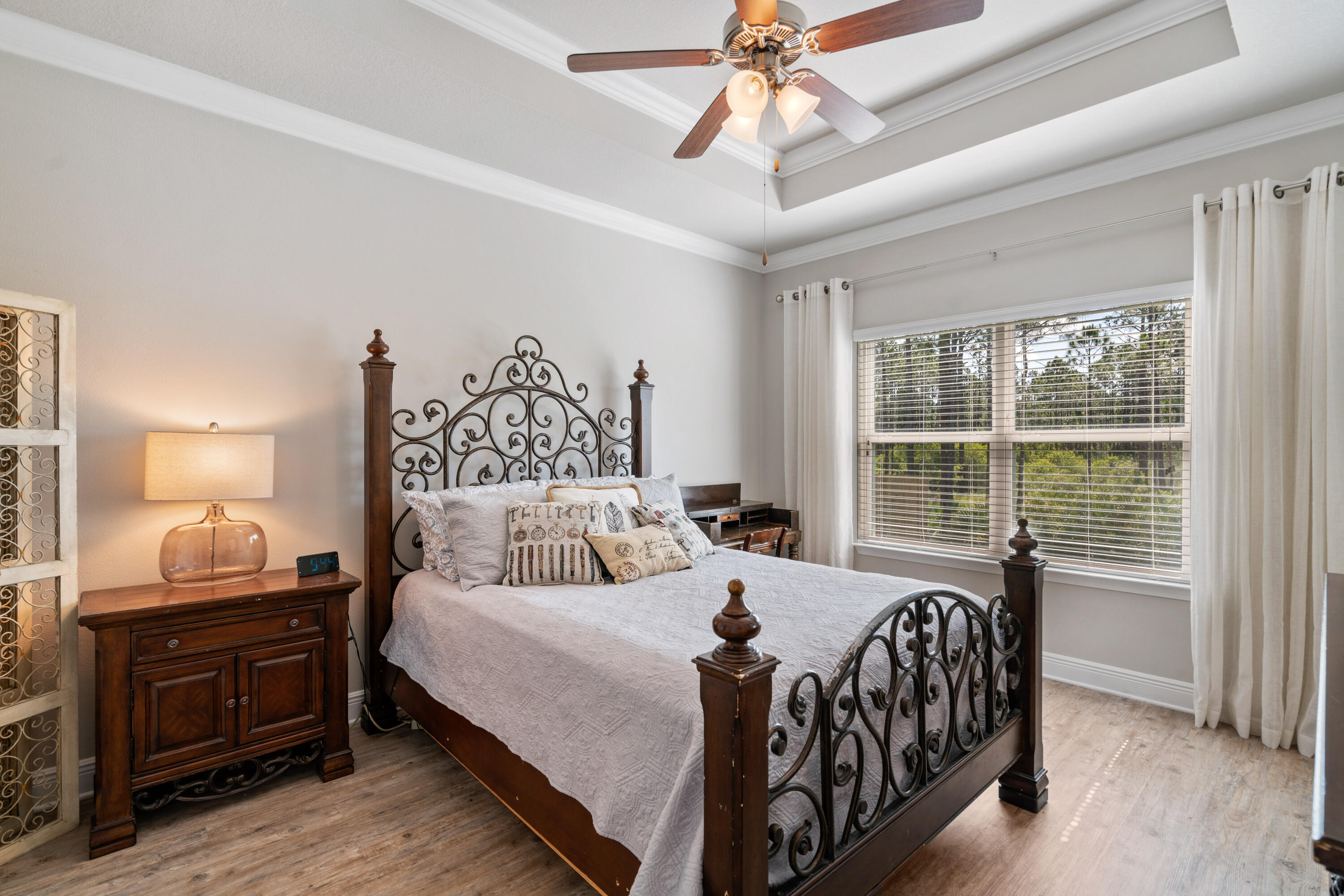 Furnished bedroom with an ornate four-poster bed, tray ceiling, and large curtained window.