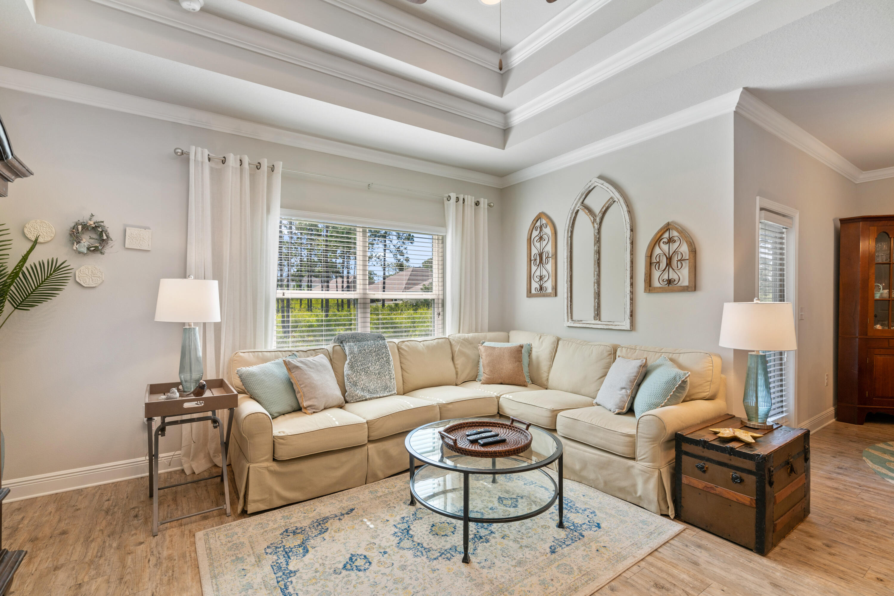 Furnished living room with a cream sectional, round glass coffee table, and tray ceiling.