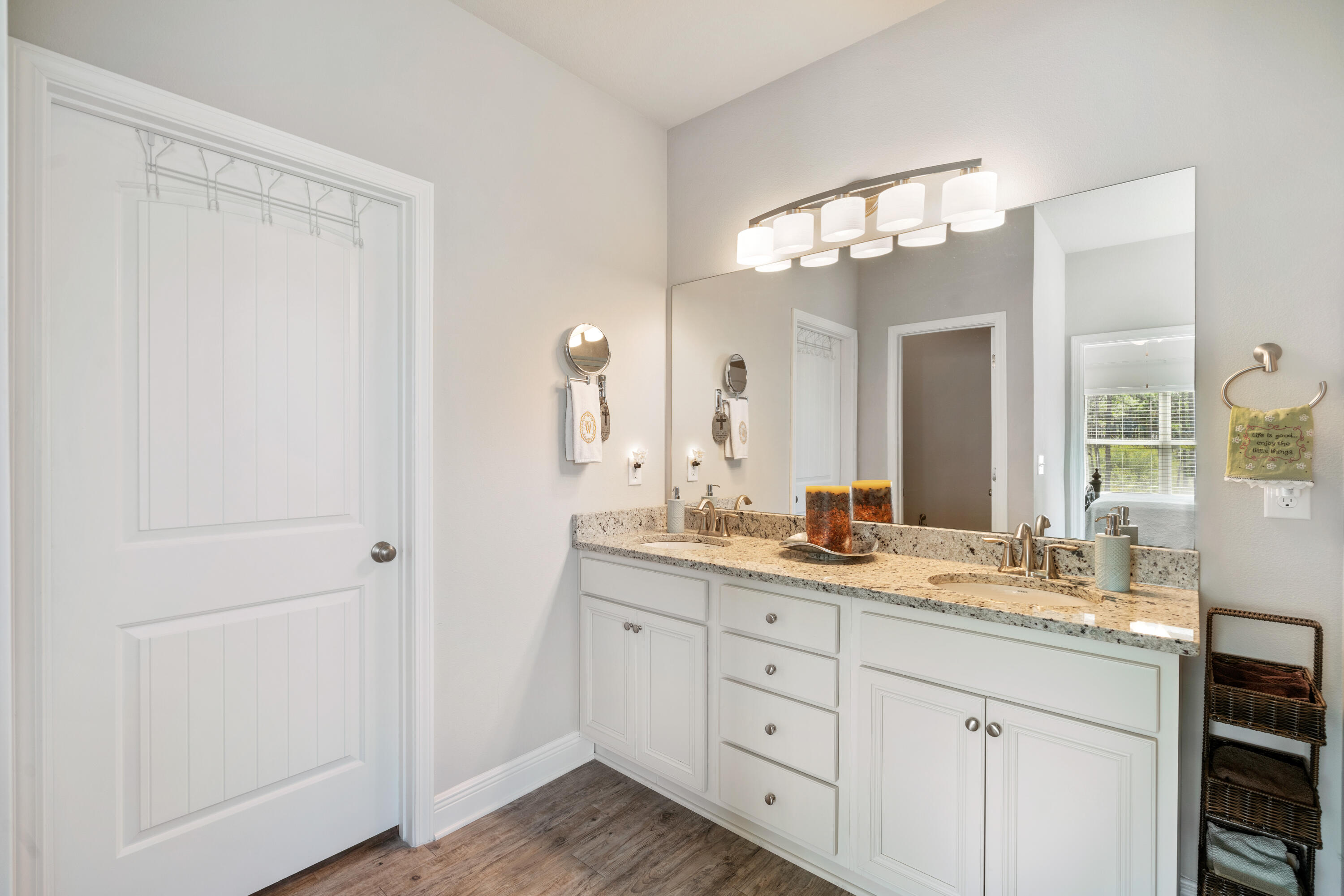 Bathroom with a white double-sink vanity, granite countertop, and large mirror beneath a row of lights.