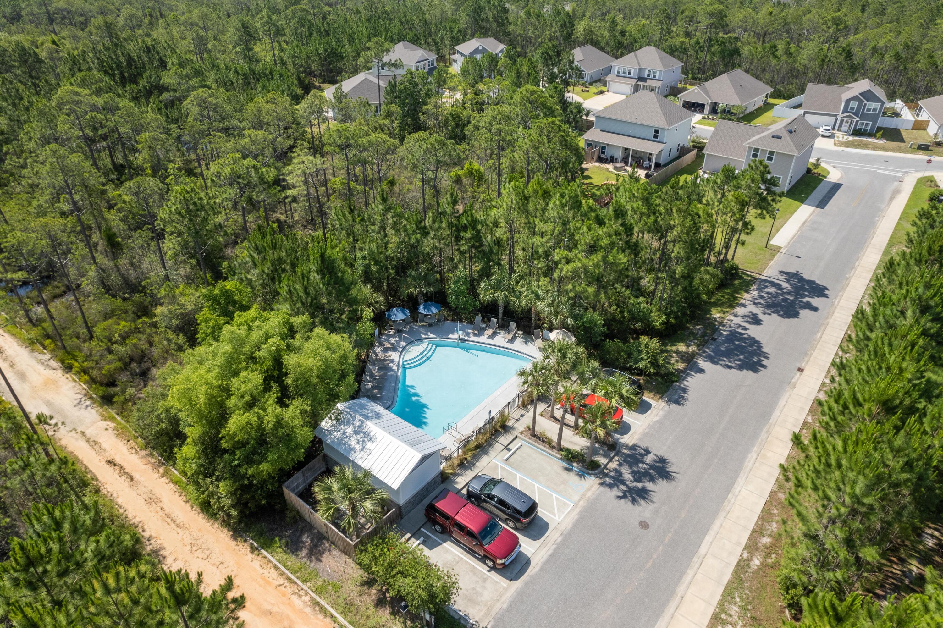 Aerial view of a neighborhood pool surrounded by trees, with homes and a street nearby.