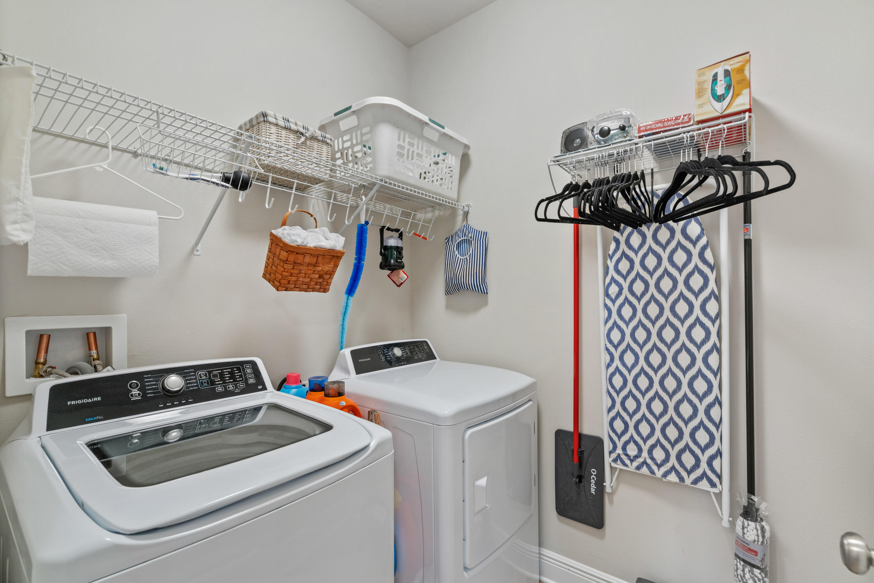 Laundry room with a washer and dryer, wire shelving, hanging hangers, and a blue-and-white drying rack.