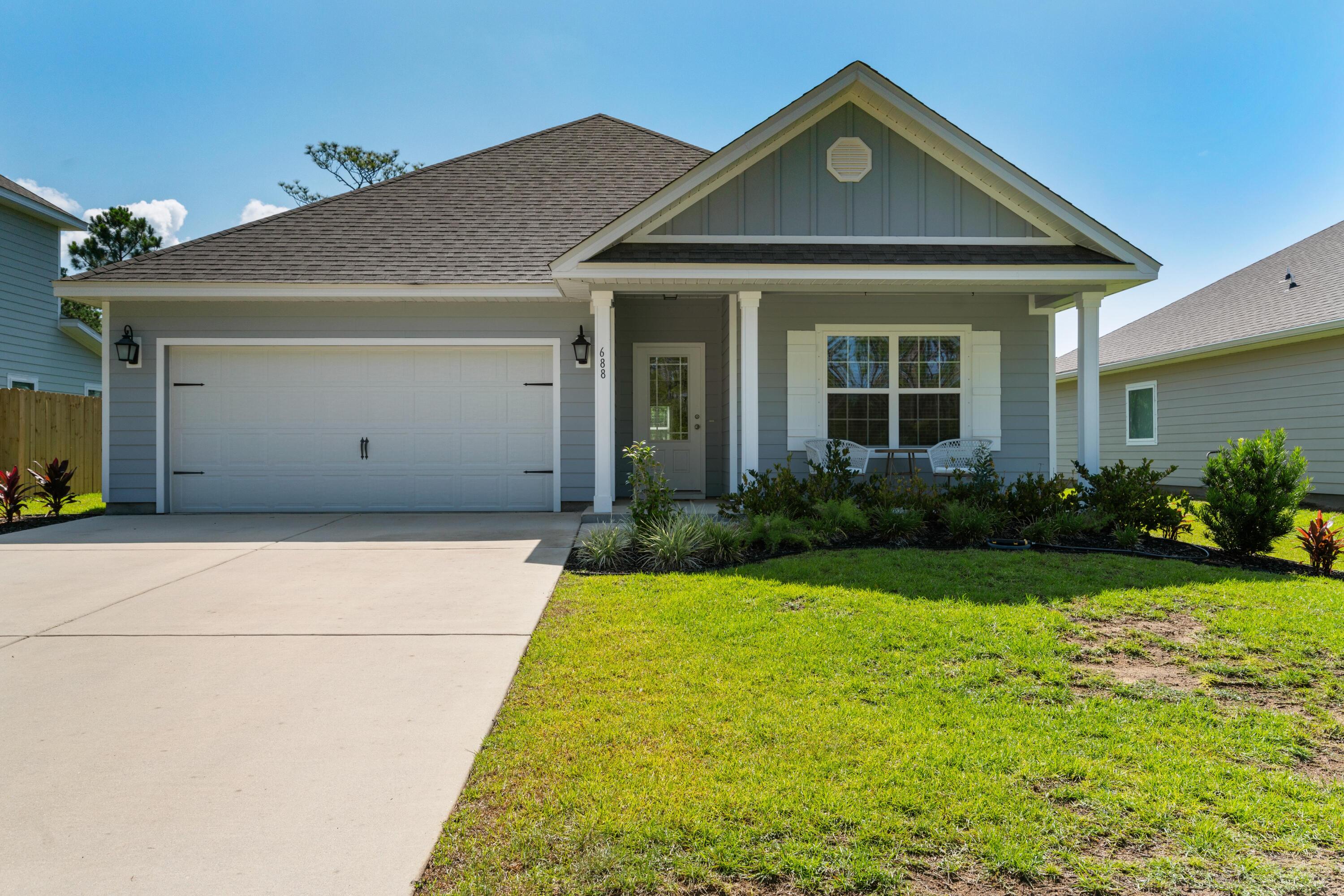 Gray single-story home with white trim, a covered porch, landscaped lawn, and wide driveway.