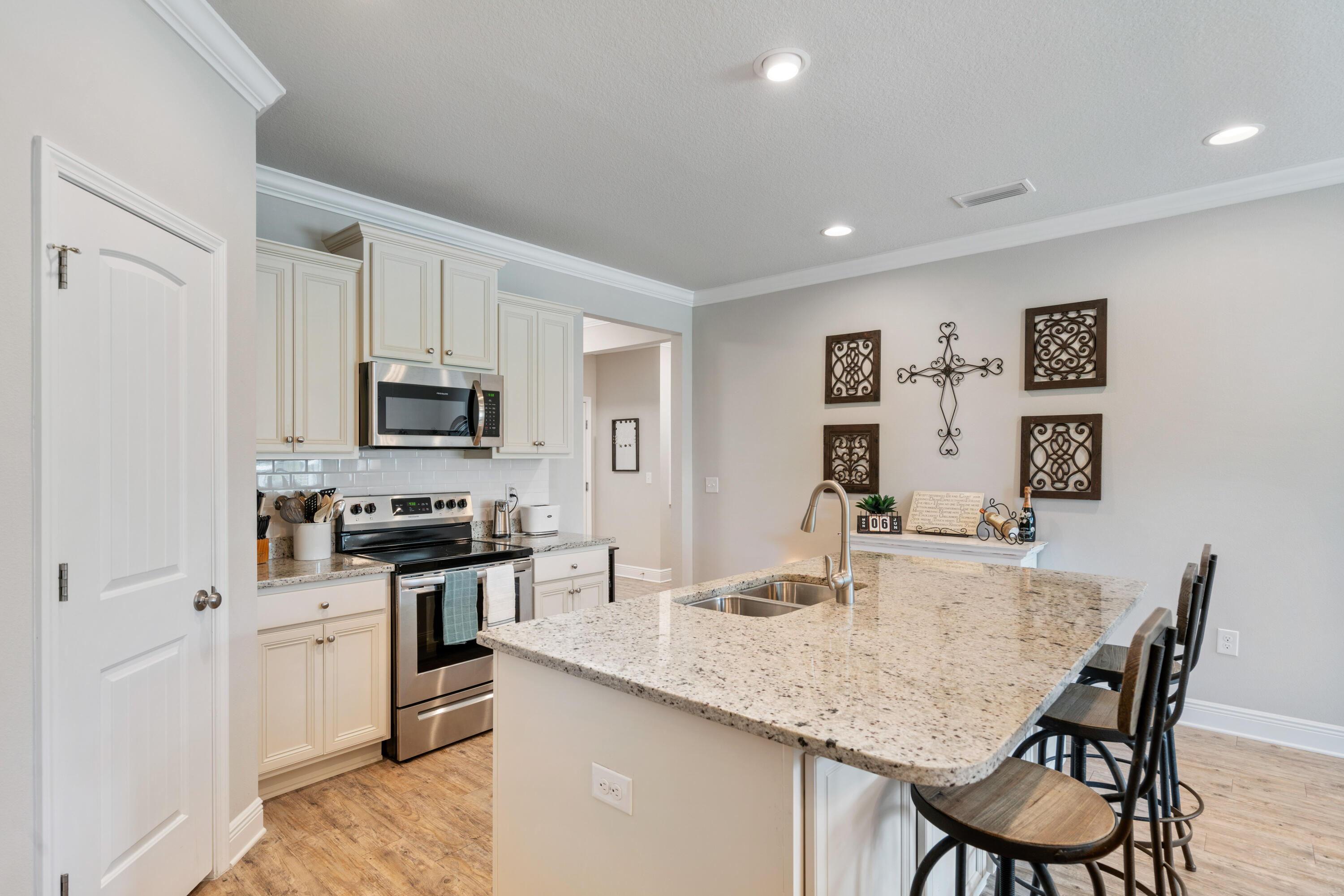Kitchen with a large granite island, undermount sink, and dark bar stools beside white cabinets.