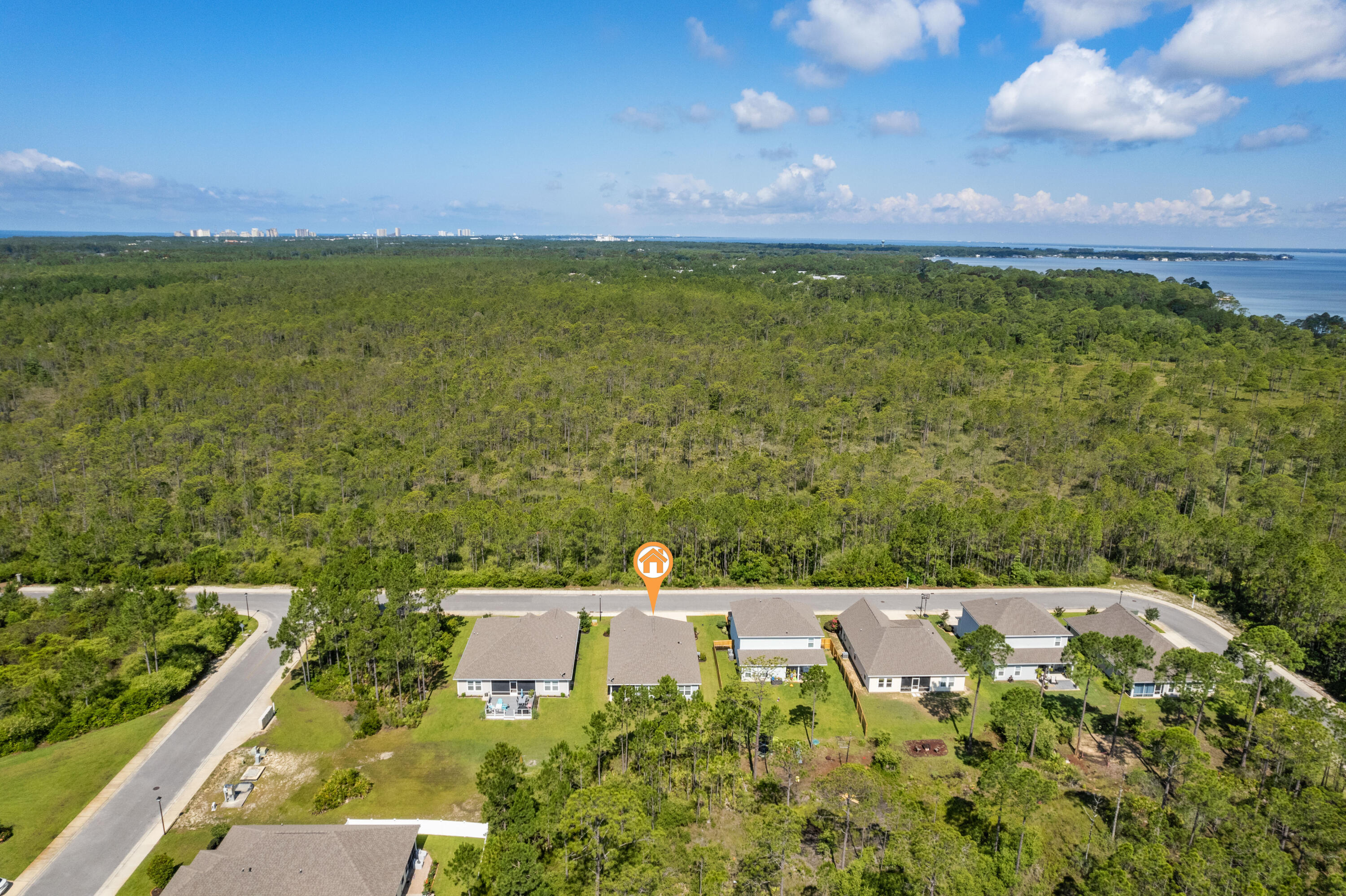 Aerial view of the marked home, with dense woodland and water beyond the neighborhood.
