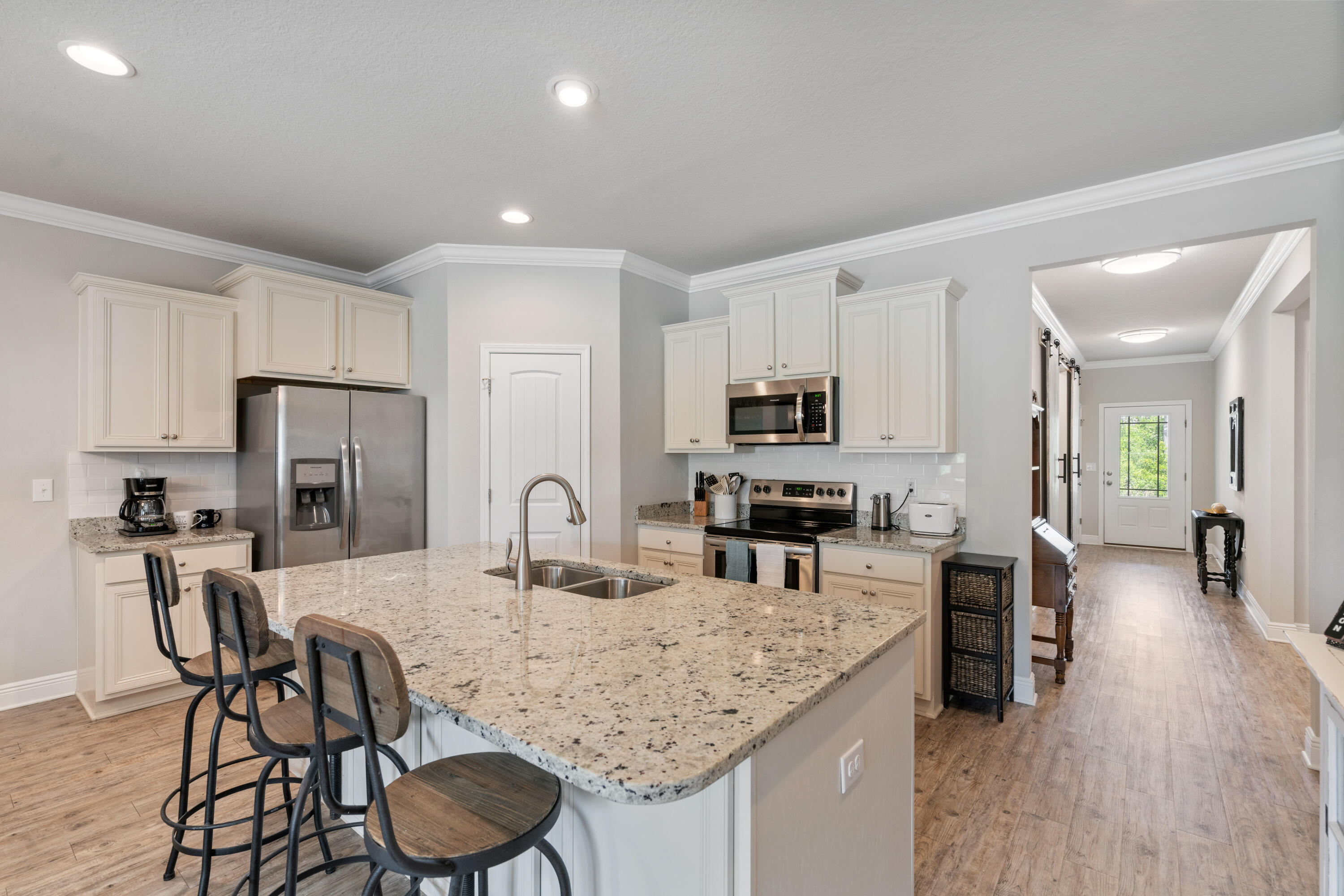Kitchen with a large granite island and bar stools, white cabinets, and stainless steel appliances.