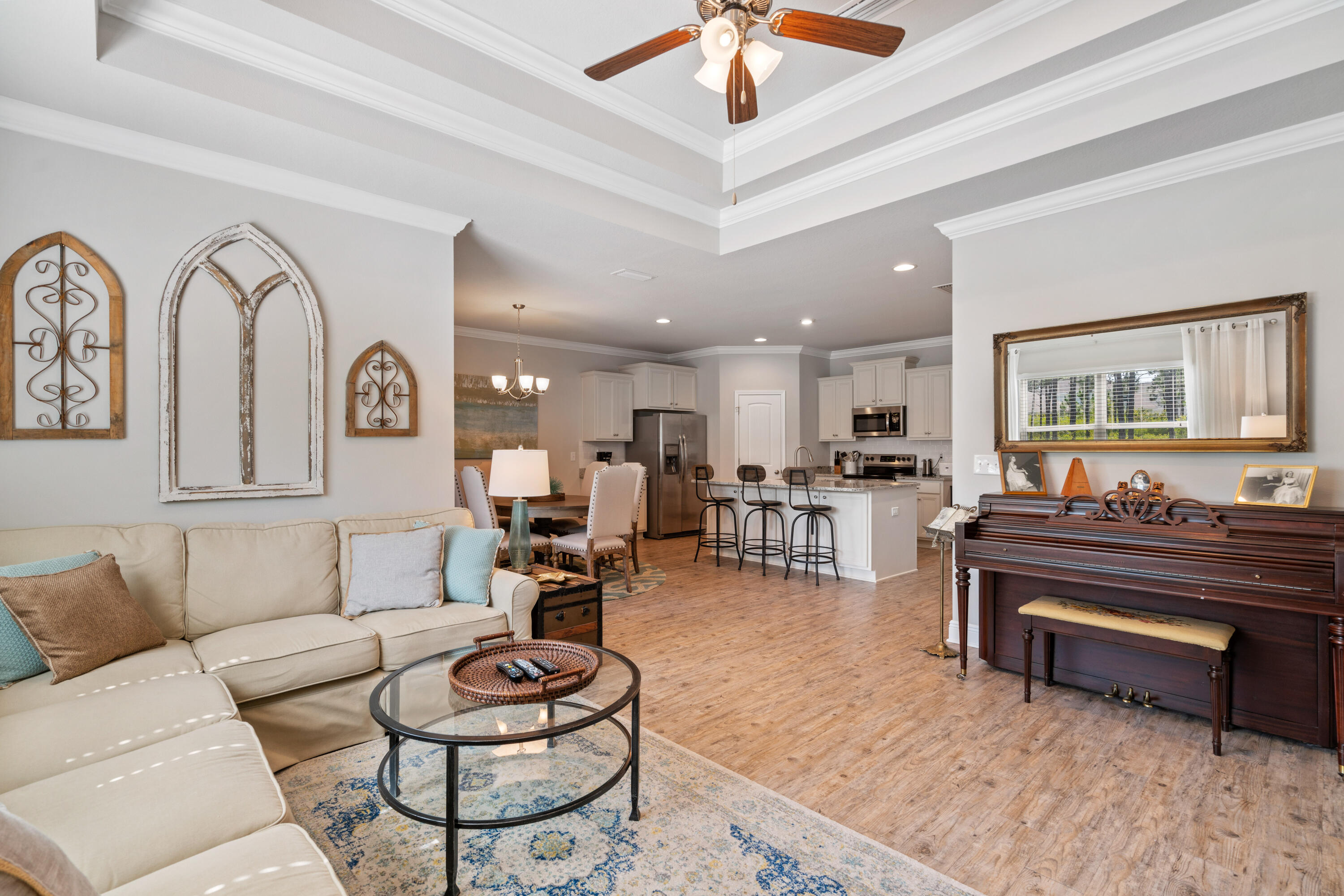 Open-plan living room and kitchen with a cream sectional, white cabinetry, and an upright piano.