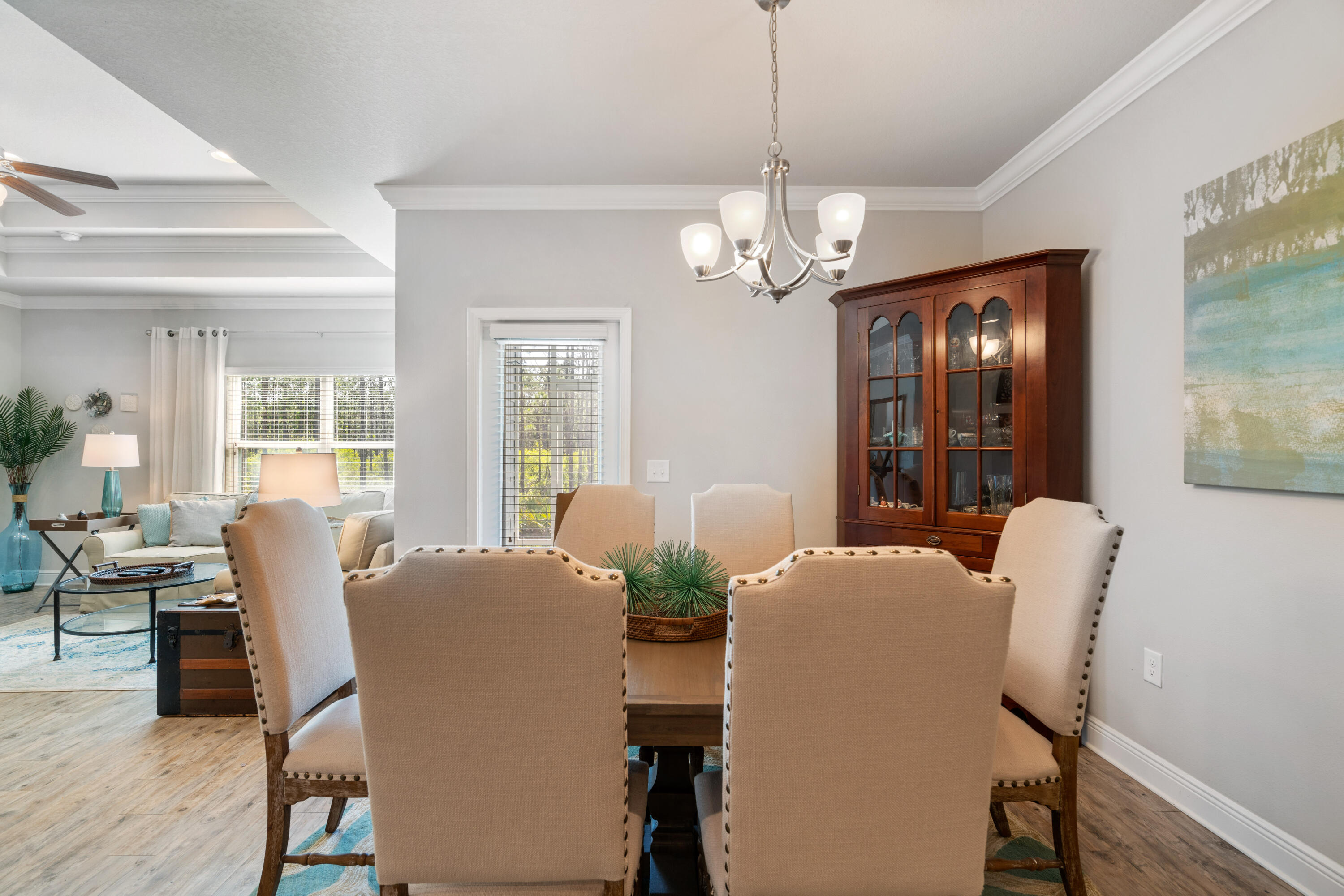 Dining room with beige upholstered chairs, a glass-front china cabinet, and a chandelier.