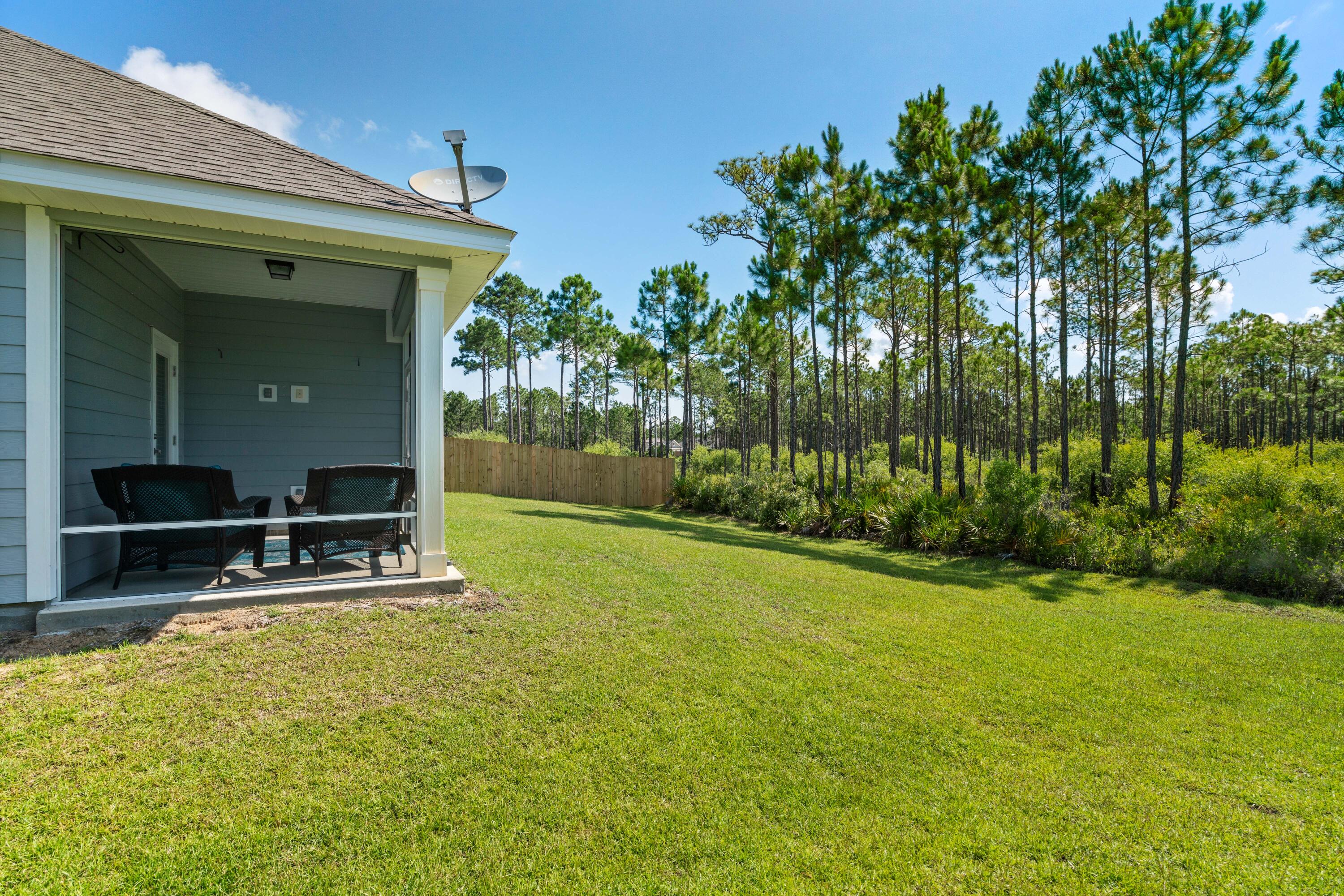 Home’s screened porch overlooks a broad lawn bordered by a wooden fence and pine trees.