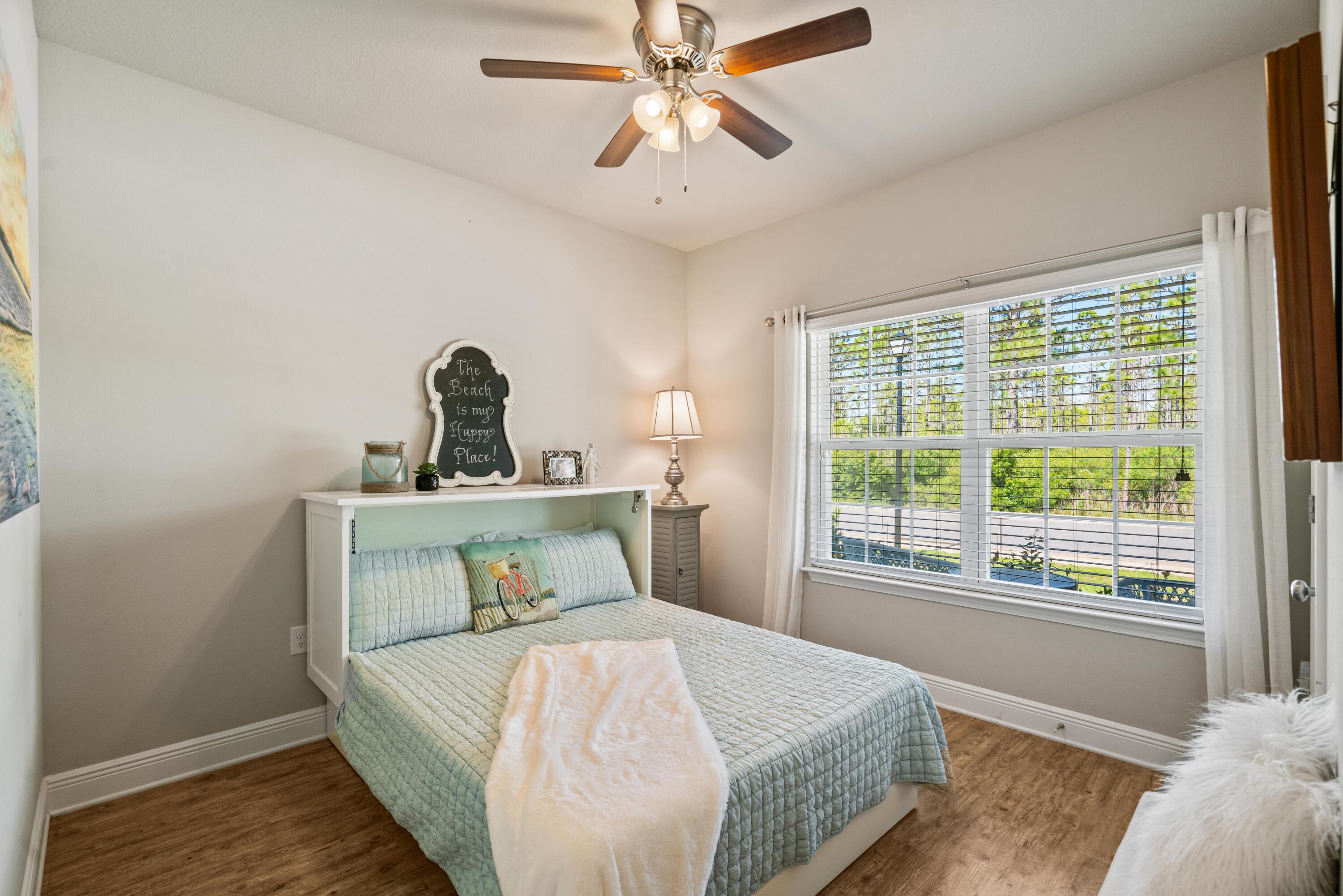 Bedroom with pale aqua bedding, a white throw, and a large window overlooking trees.