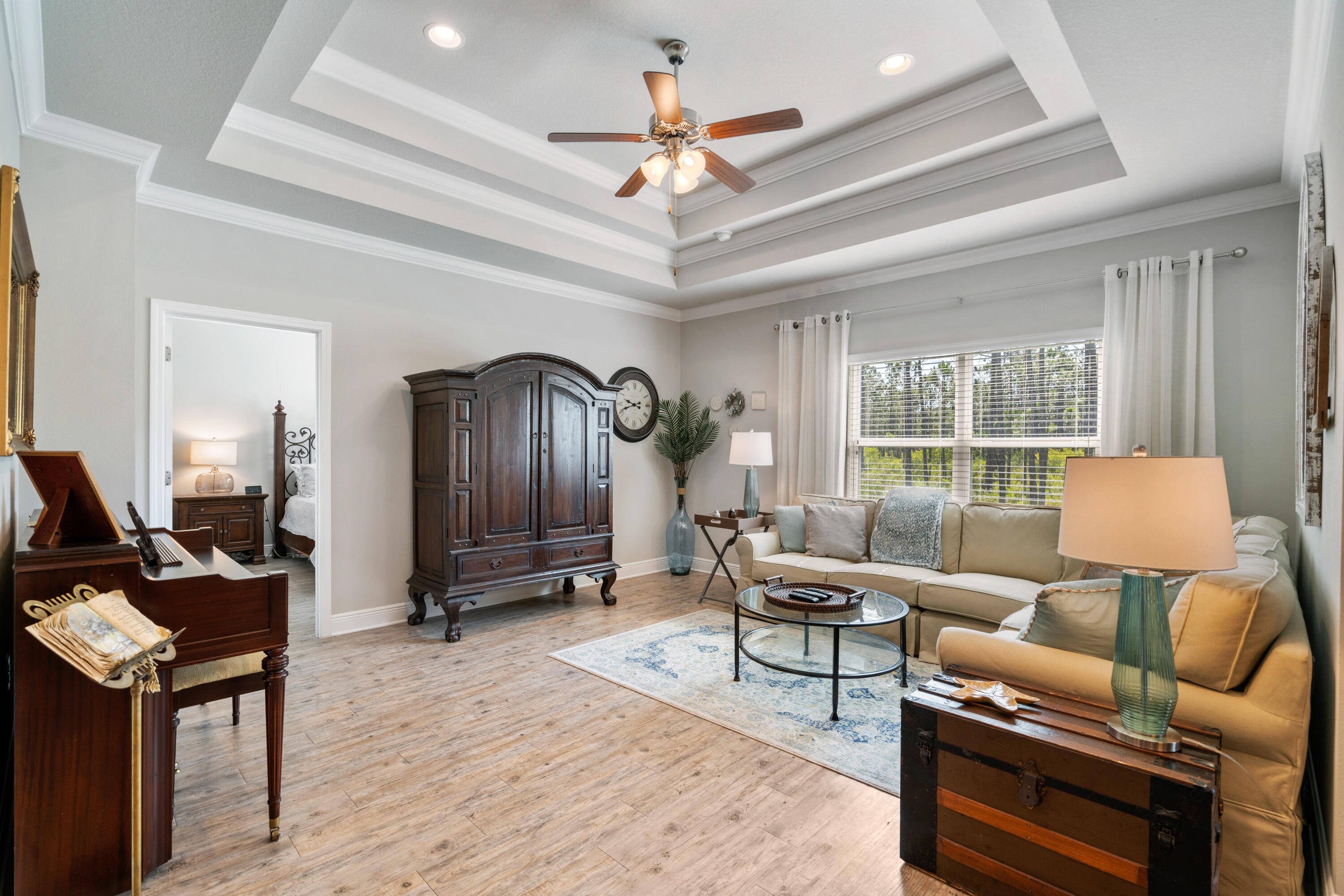 Living room with a beige sectional, antique wooden armoire, tray ceiling, and a view of greenery.