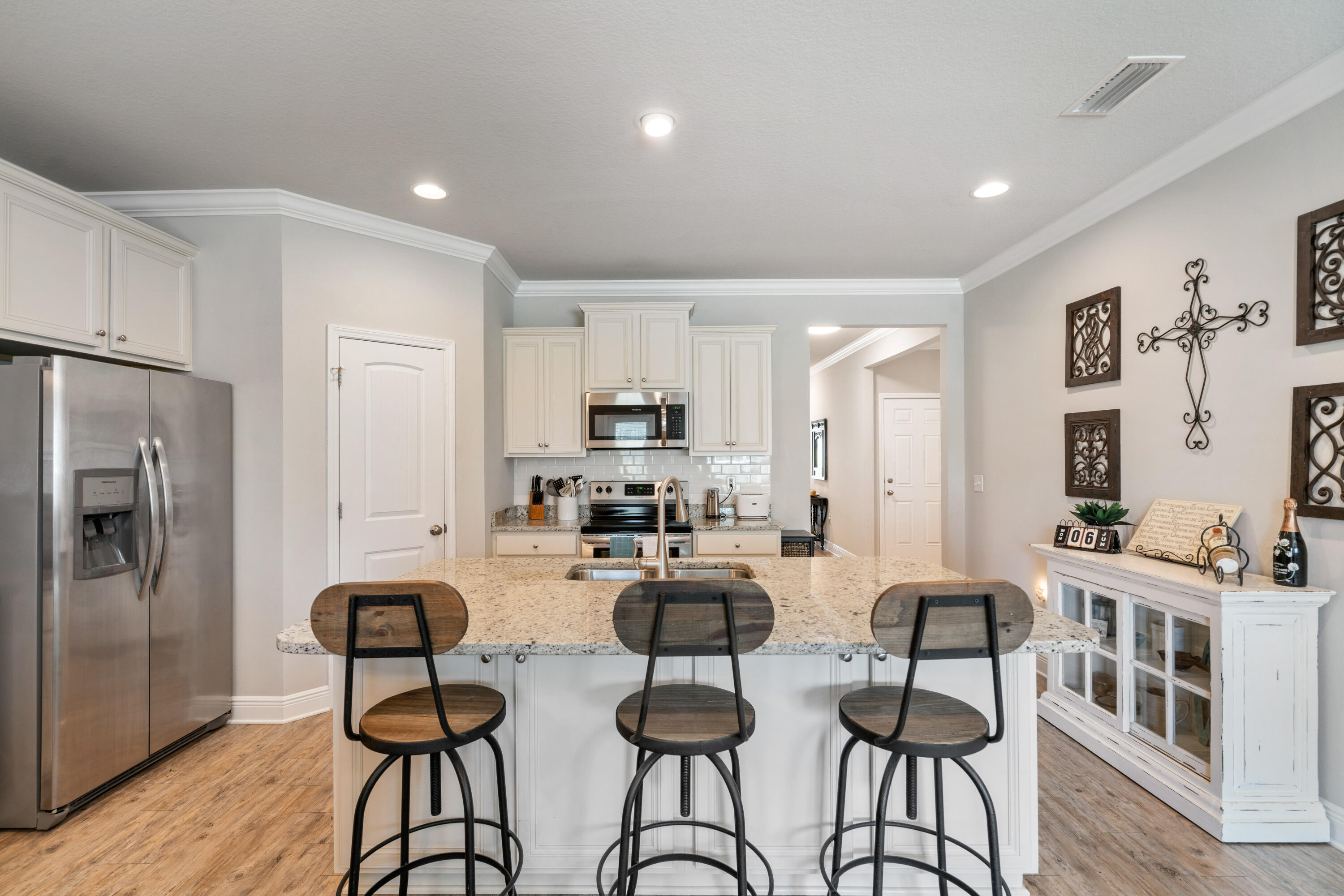 Kitchen with a granite island and three bar stools, white cabinetry, and stainless steel appliances.