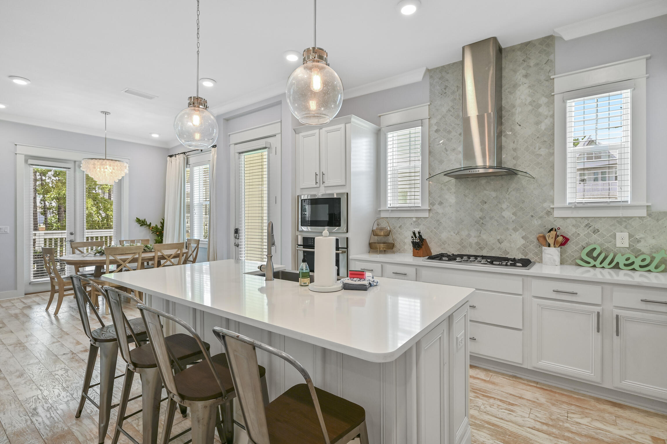 Kitchen and dining area with a large white island, patterned backsplash, and glass doors.