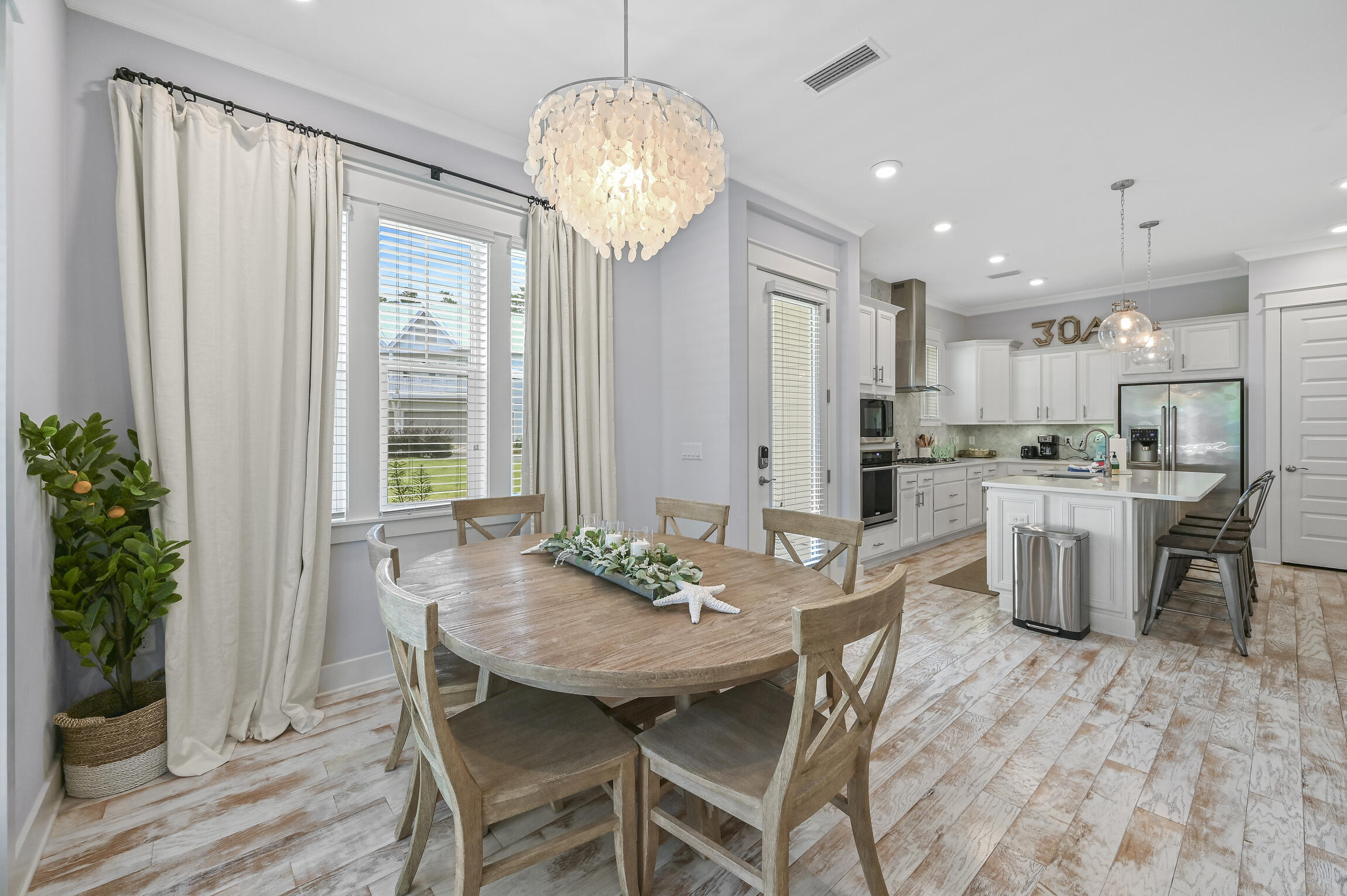 Dining area with a round wood table beside a bright white kitchen and island.